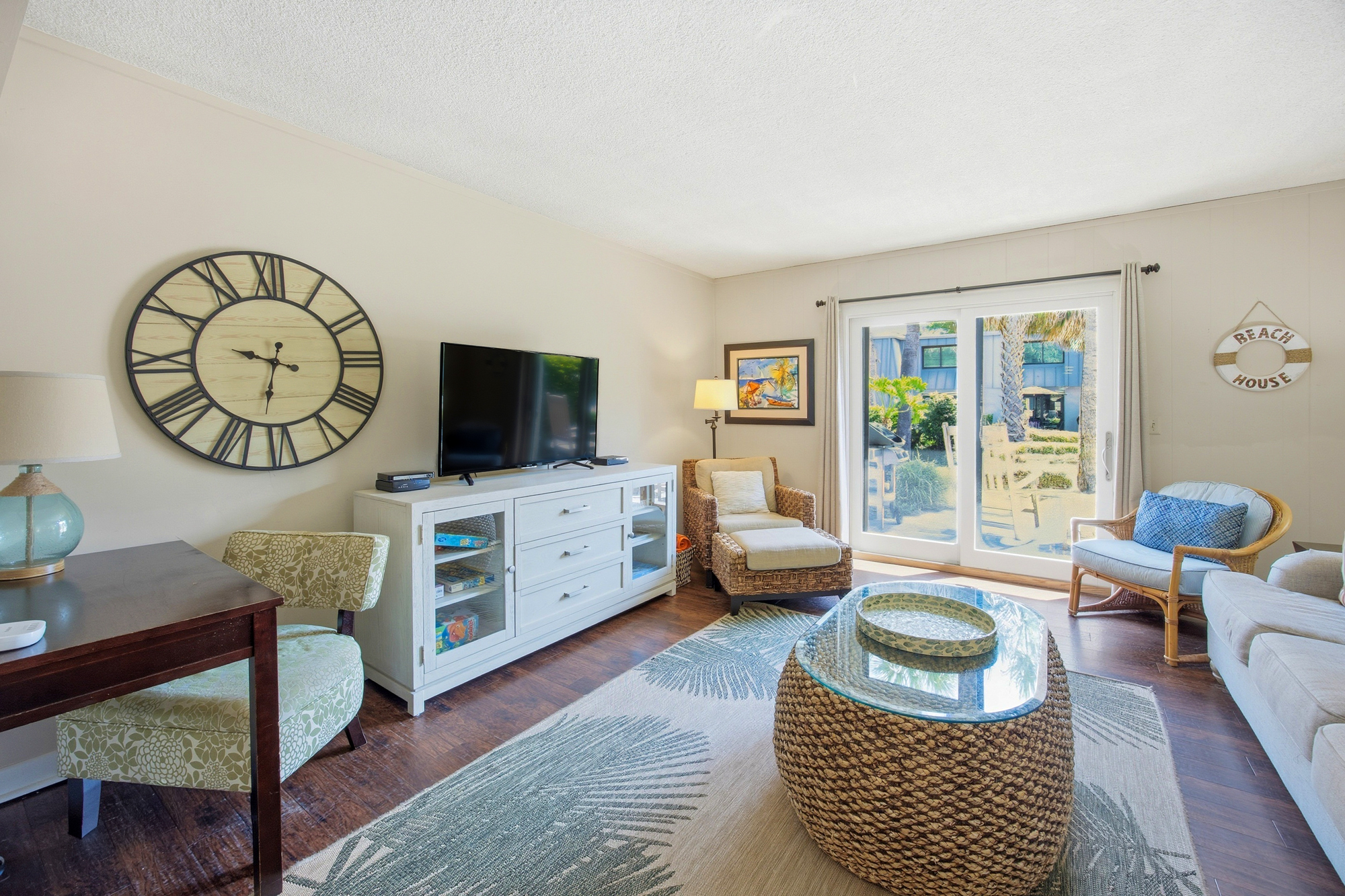 Coastal textures meet breezy charm in this airy living room, where jute accents and seaside decor create a tranquil mood. Large glass doors pull in a bright daytime glow, connecting the cozy seating area to the garden views just steps away.