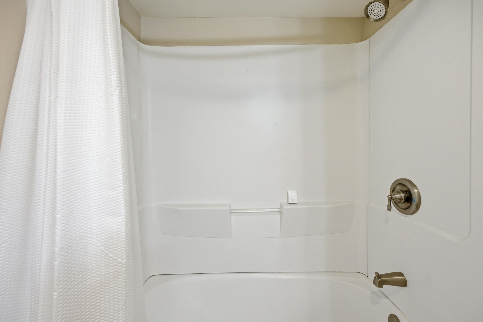 Pristine white surfaces and brushed nickel fixtures create a bright, refreshing space for your morning routine. A textured curtain adds a soft touch to this clean and quiet corner, perfect for a long soak or a quick rinse before your day begins.