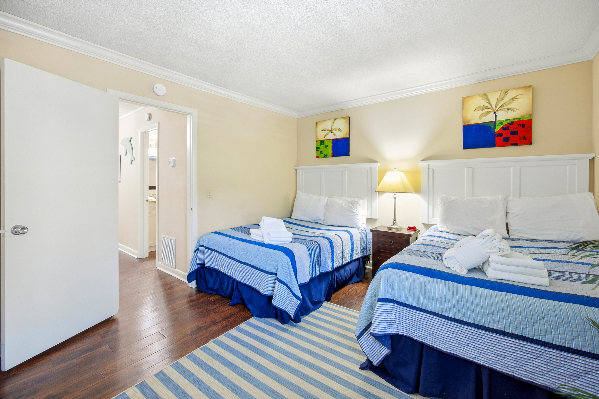 Nautical blue linens and matching stripes bring a coastal charm to this twin bedroom. A golden lamp glow spills across the mahogany floors and crisp headboards, creating a peaceful corner for a restful night after a day of exploring.