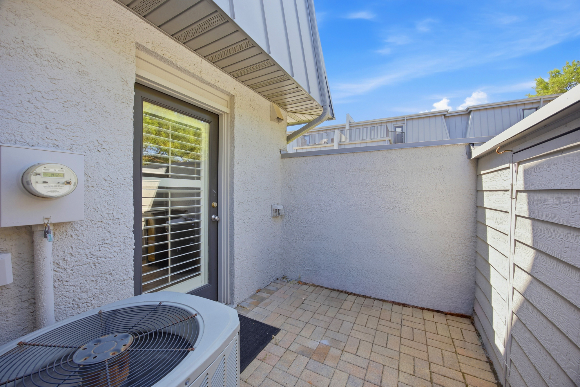 Sun-drenched paving stones create a quiet, private outdoor corner perfect for a breath of fresh air. This secluded patio space offers a peaceful spot to pause under the clear blue horizon.