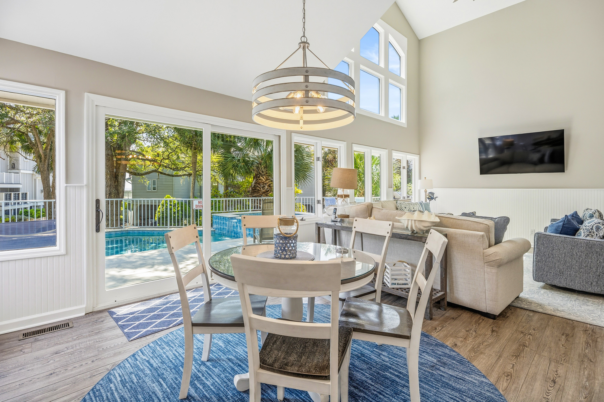 Vaulted ceilings and towering windows flood this airy dining space with a soft afternoon glow. Coastal textures of wood and glass pair beautifully with the view of your private poolside patio just beyond the sliding doors.
