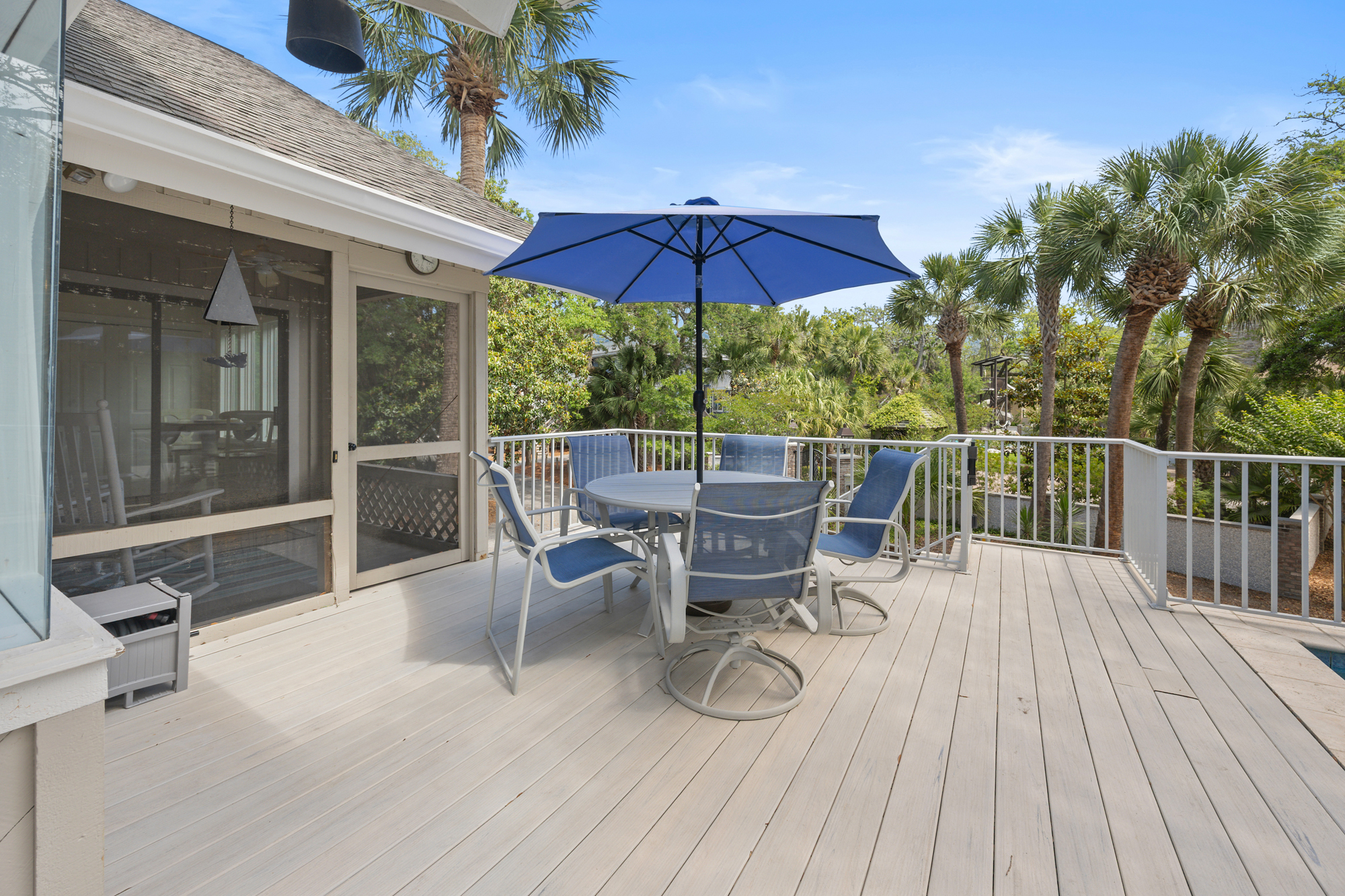 Weathered timber planks lead to a breezy dining nook shaded by a deep indigo umbrella. Towering palms frame this elevated porch, where quiet mornings and golden afternoon light create a perfect spot for coffee or open-air meals.