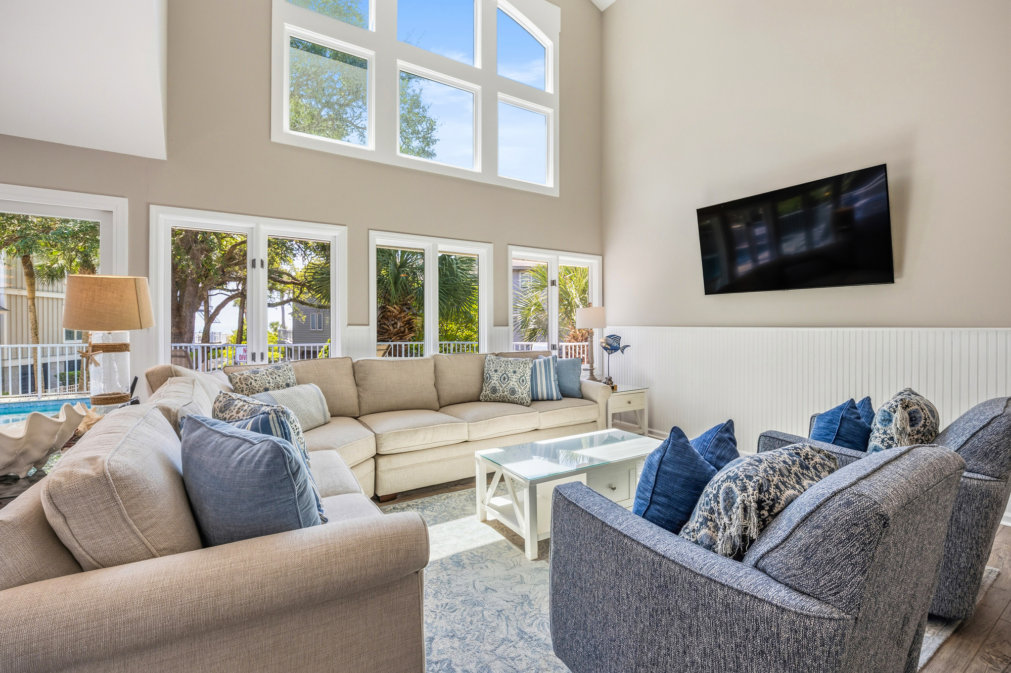 Soaring ceilings and a wall of windows fill this airy lounge with a soft afternoon glow. Denim-toned fabrics and textured pillows offer a comfortable spot to gather, while views of swaying palms bring the outdoors inside.