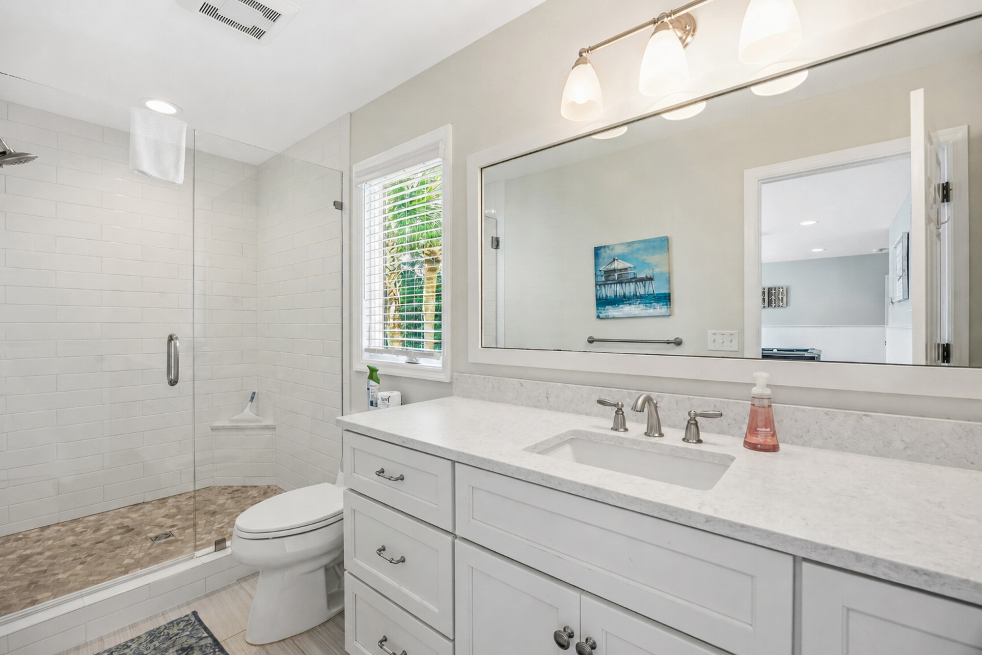 Natural stone textures and cool marble surfaces define this airy bathroom. Warm vanity lighting and a glass-enclosed shower create a serene, spa-like atmosphere for your morning routine.