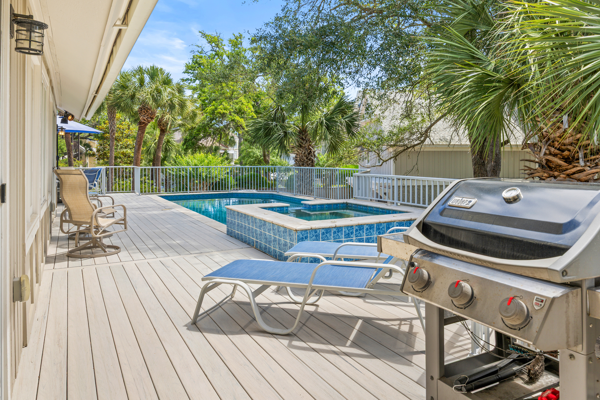 Smooth timber decking leads toward a sparkling pool and spa, where leafy trees provide a canopy of natural shade. Fire up the grill for an afternoon barbecue on this spacious terrace, perfectly designed for slow days under a clear sky.