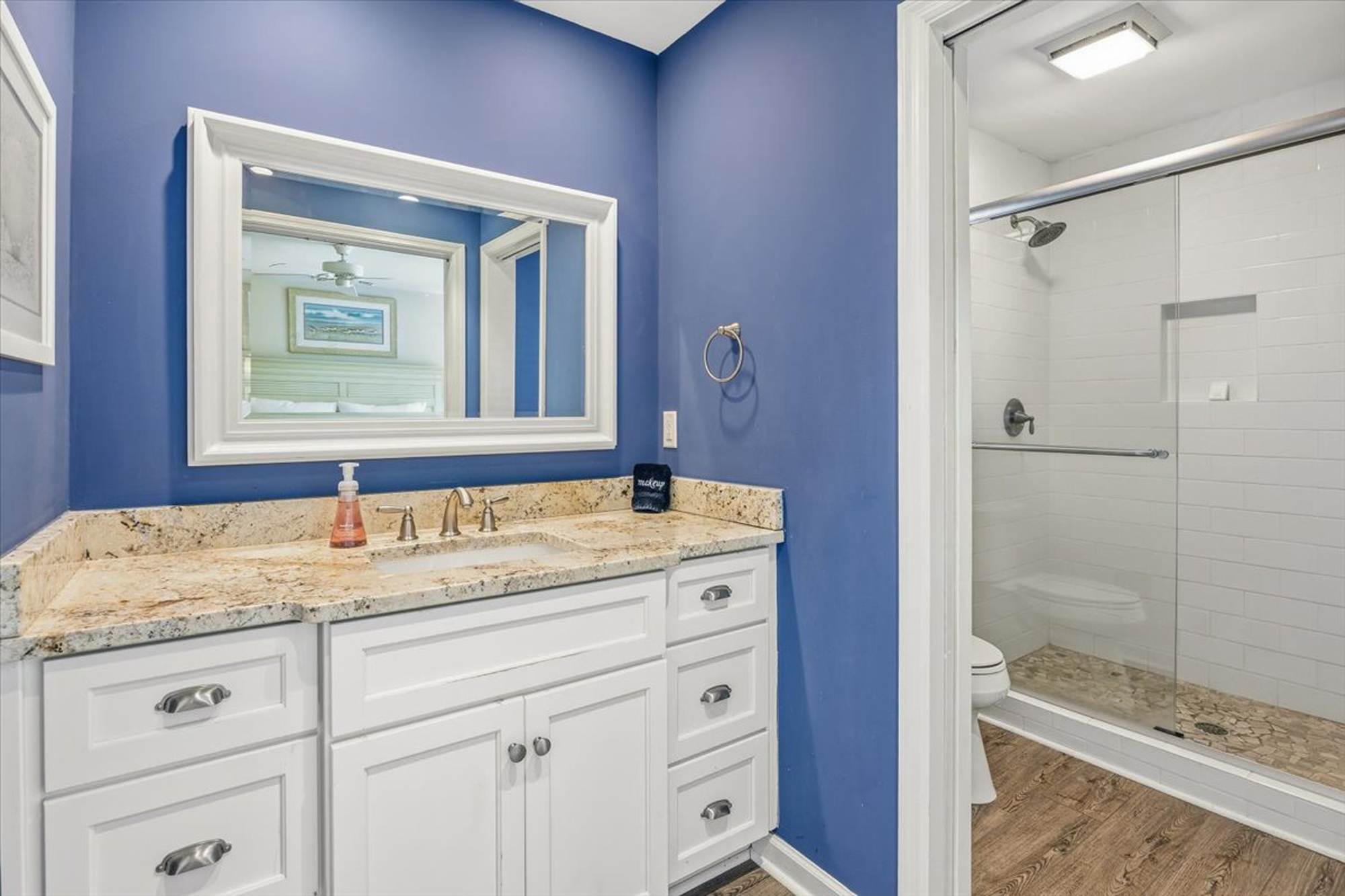 Sapphire walls provide a bold backdrop for this refreshment space, anchored by a granite vanity and a clean, glass enclosed shower. Earthy stone tiles underfoot add a spa like texture to your morning routine.