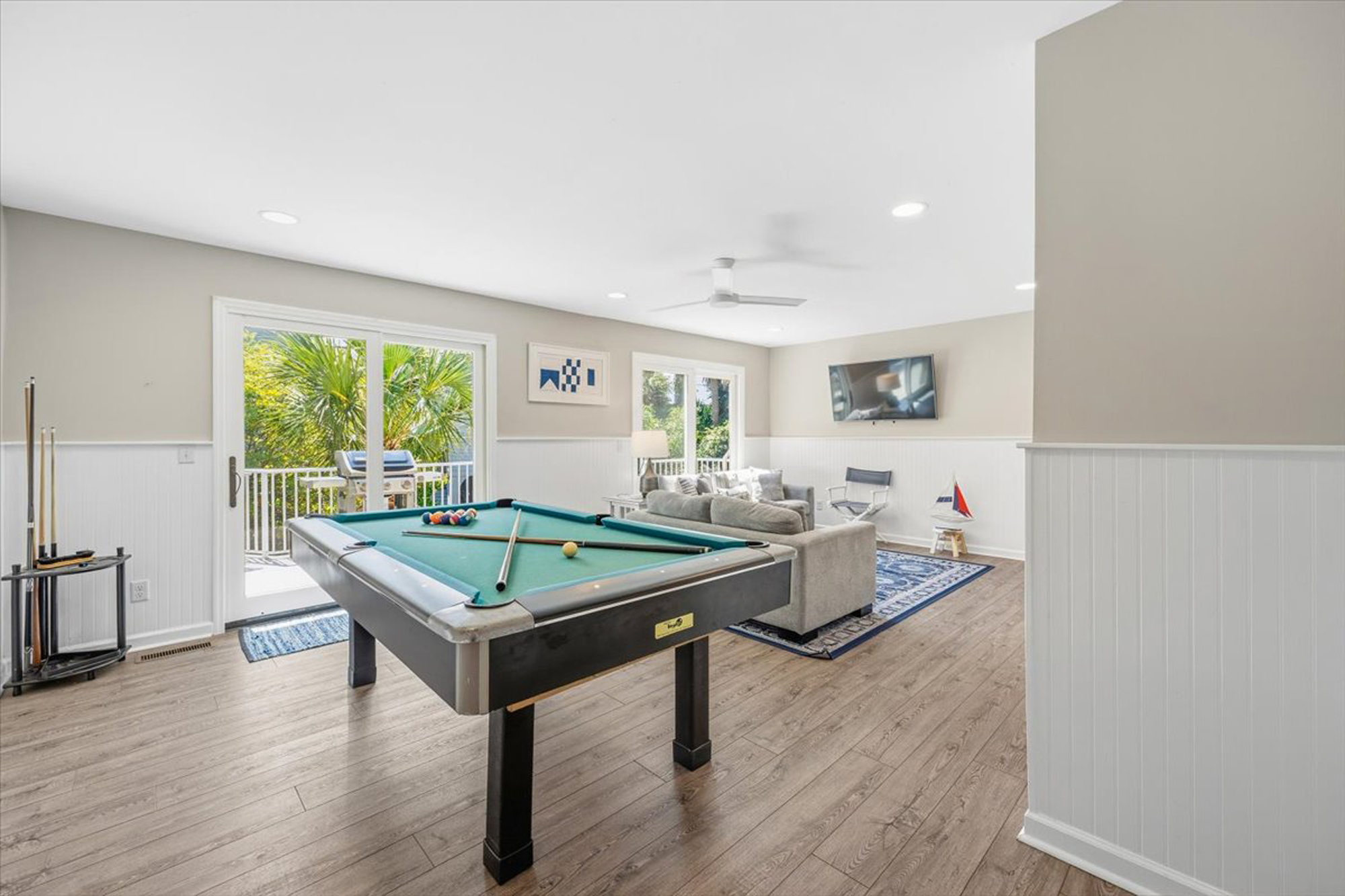Grainy wood textures and crisp wainscoting frame this airy game room, where a classic pool table awaits a friendly match. Large glass doors draw in the gentle garden glow, connecting the cozy lounge to the lush greenery just outside.