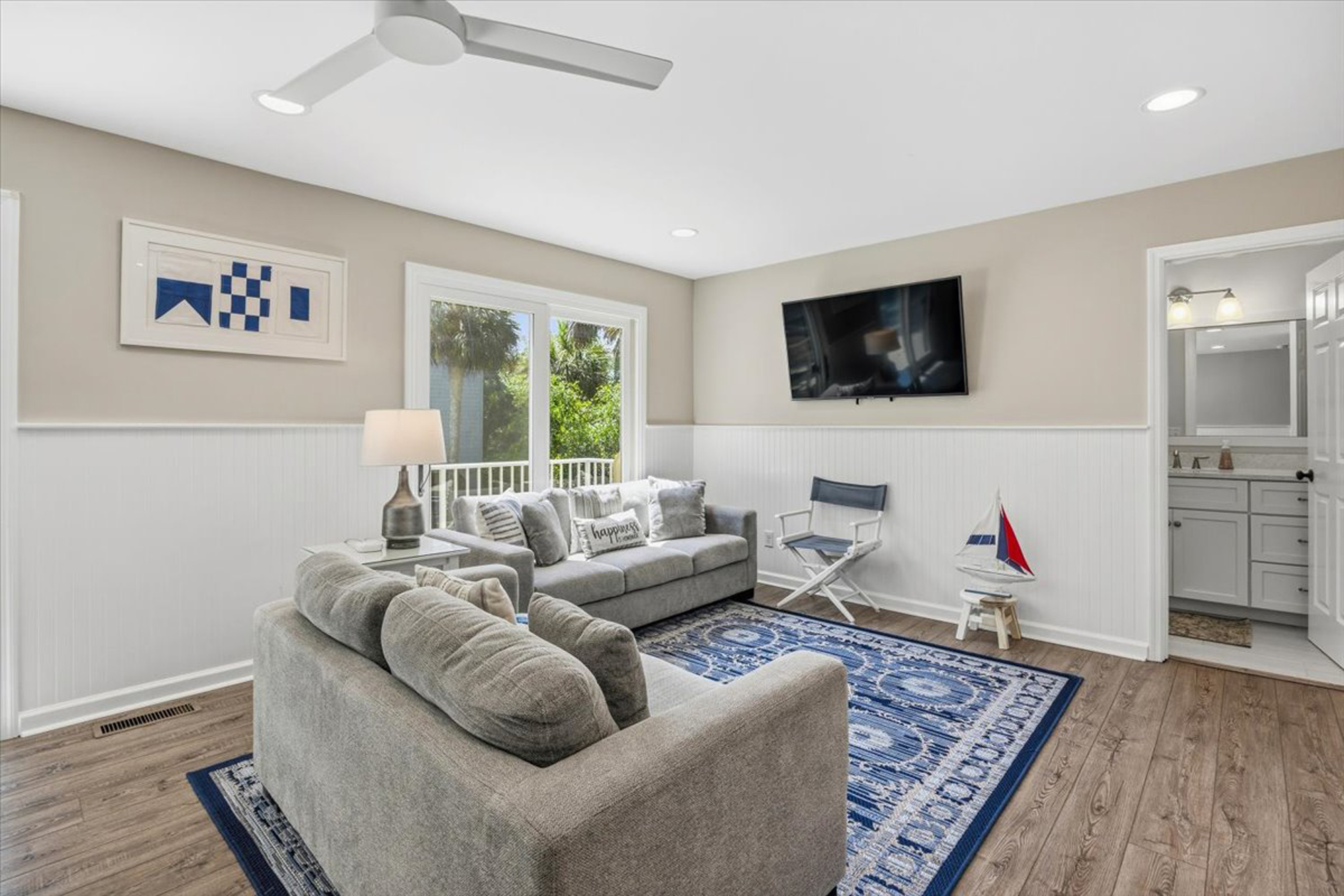 Navy blue patterns ground this airy lounge, where beadboard walls and linen textures create a serene maritime mood. Sliding glass doors pull in leafy views, filling the room with a gentle morning glow.