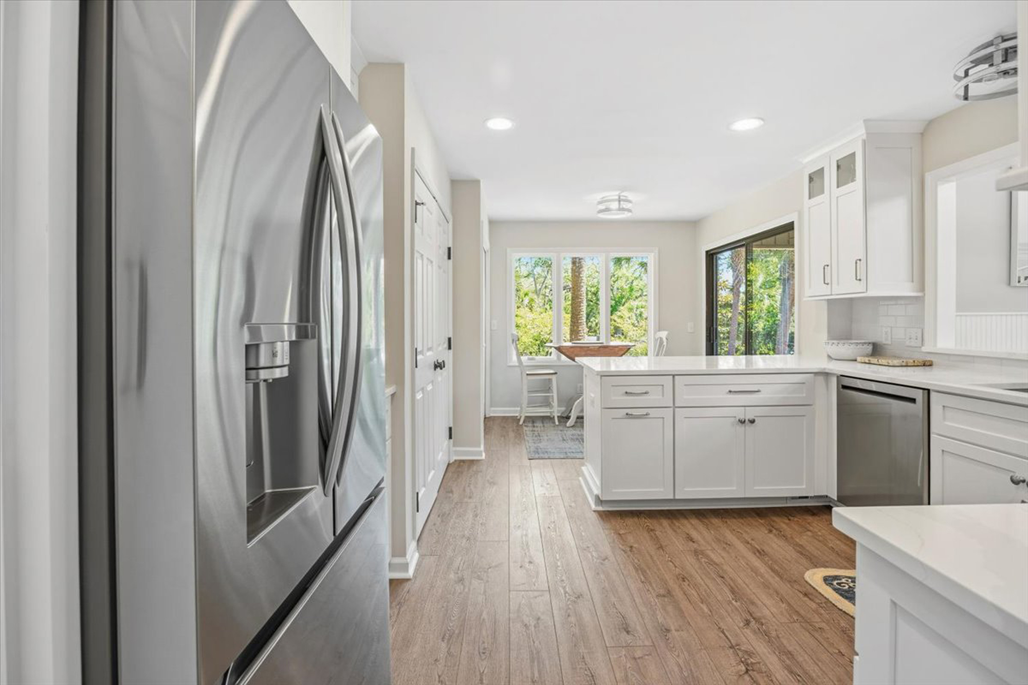 Stainless steel appliances and snowy cabinetry create a clean, modern chef’s space. Afternoon glow pours through the windows, highlighting the warm wood tones and making this airy kitchen the heart of the home.
