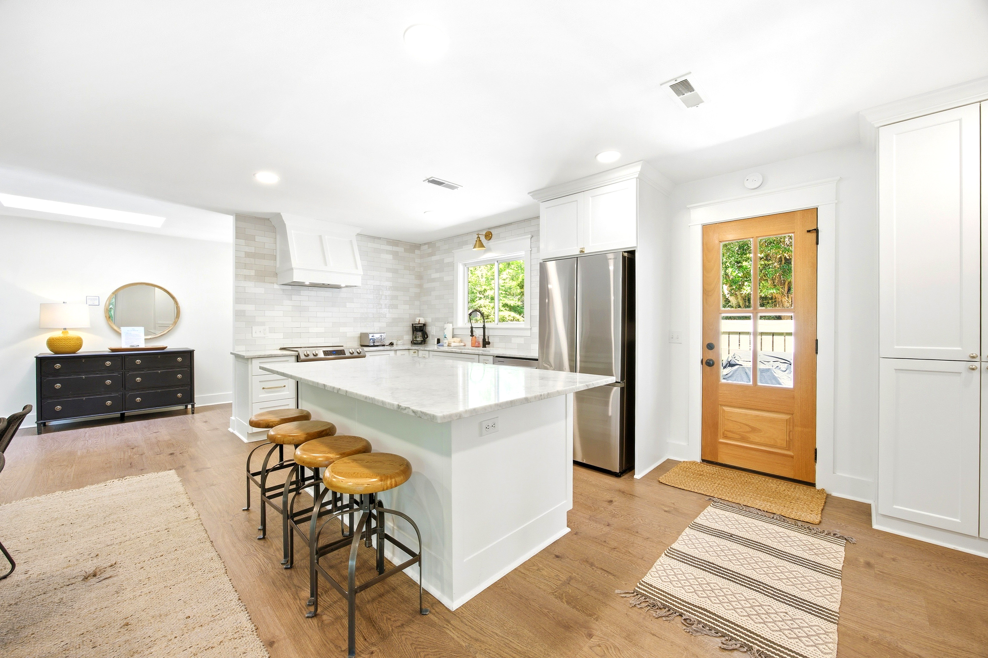 Honey-hued oak floors meet a vast marble island in this airy kitchen, where golden afternoon rays pour through the glass door. Polished steel and industrial stools offer a sleek yet cozy spot to gather for morning coffee and conversation.