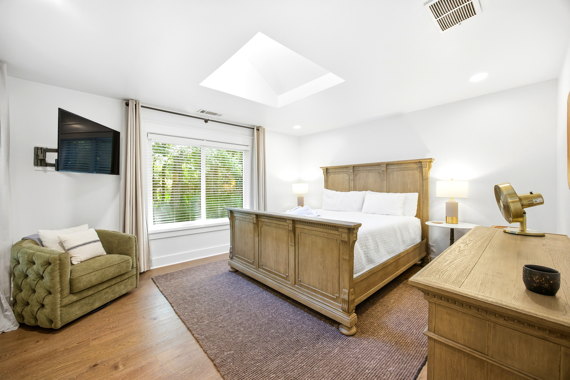 Natural radiance pours through the skylight, illuminating the heavy oak bed and soft, mossy armchair. Crisp white linens and warm wood tones create a bright, airy sanctuary for deep rest and slow mornings.