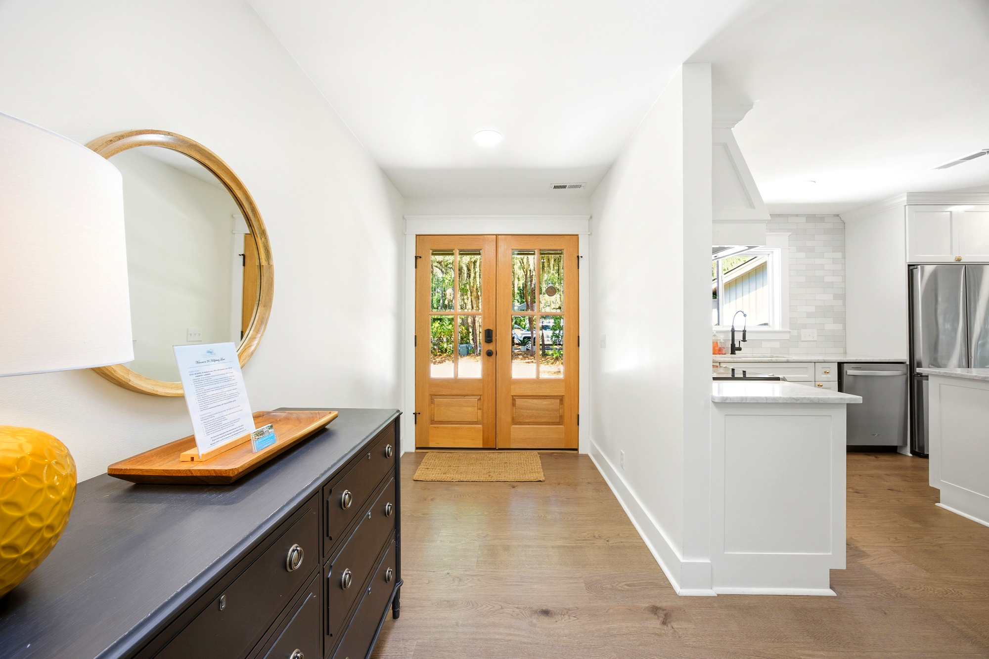 Timber double doors pull the outdoors in, illuminating a bright entryway and open kitchen. Crisp walls and smooth wood grains create a calm, airy atmosphere that feels like a fresh start to your stay.