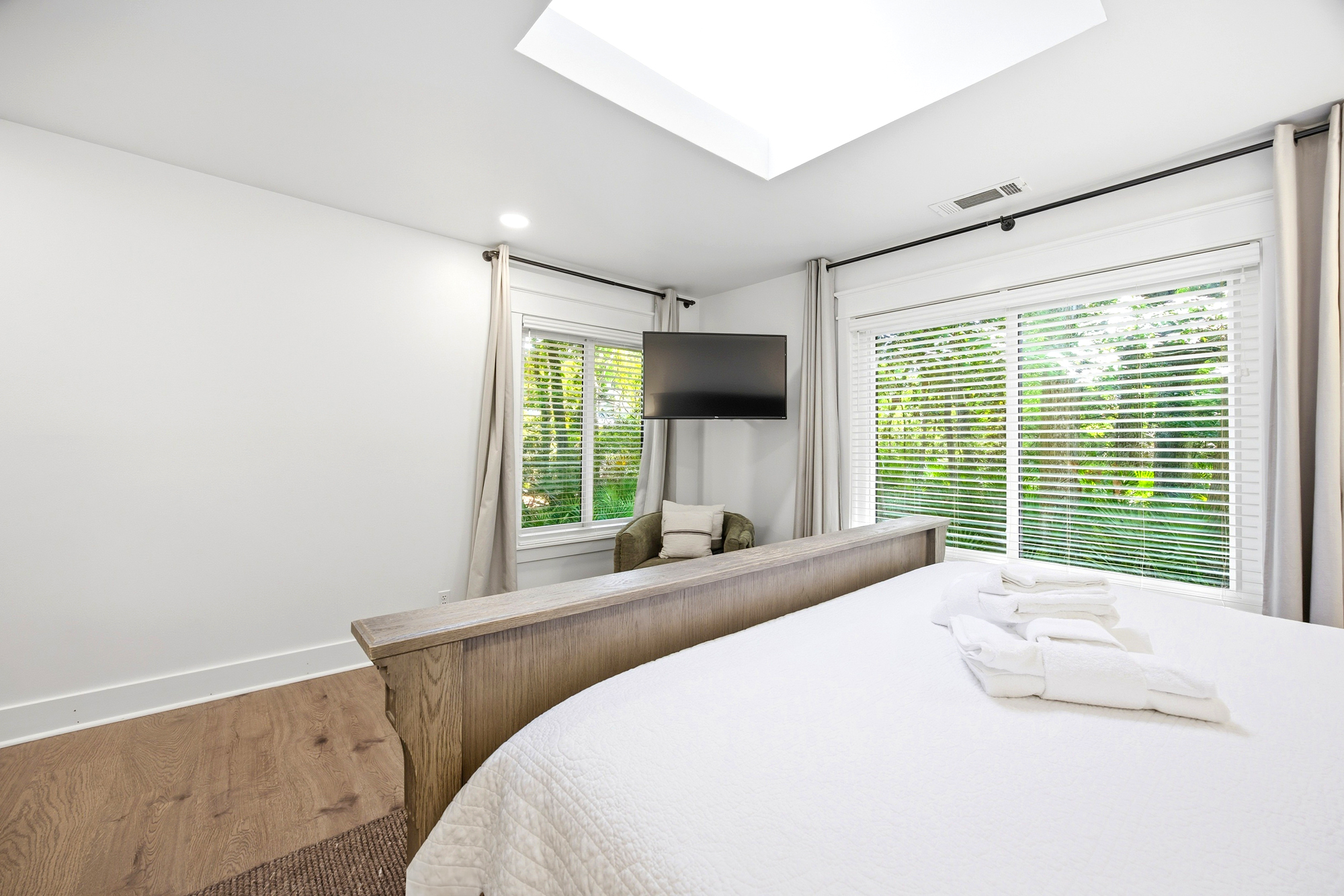 Daylight streams through a wide skylight and leafy windows, illuminating a serene suite where oak accents meet fresh linens. This airy sanctuary offers a peaceful corner for slow mornings and quiet rest among the trees.