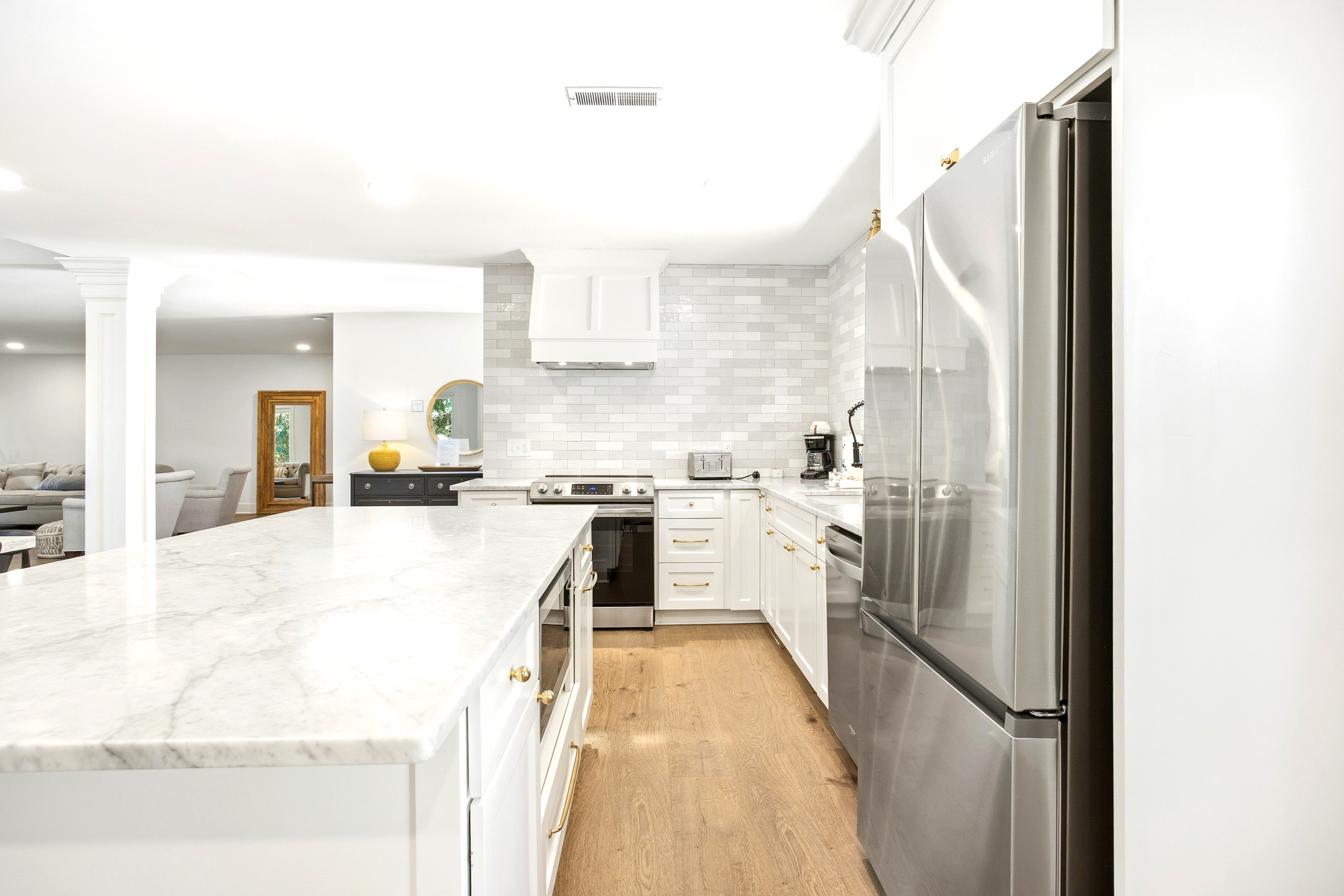 Gleaming stone countertops and crisp subway tiles create a bright, airy culinary space. Modern stainless steel appliances pair with golden hardware and light wood floors to offer a sophisticated yet cozy heart for your morning coffee.