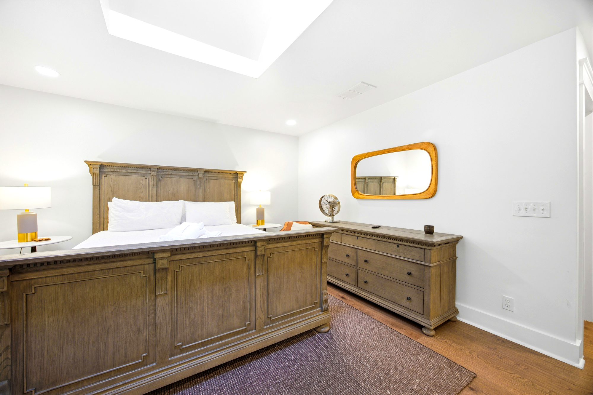 Polished wood grains and crisp linens define this serene bedroom, where a skylight pours soft daytime brightness over the king bed. A hand-carved dresser and warm textures create a grounded, peaceful space for quiet mornings.