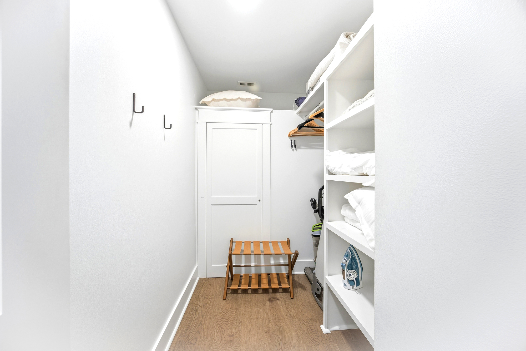 Organized shelves and a leather luggage rack offer a tidy spot to unpack, while bright walls create a clean, airy feel for your belongings. This functional nook pairs oak-toned floors with plenty of space to keep your travel essentials ready.