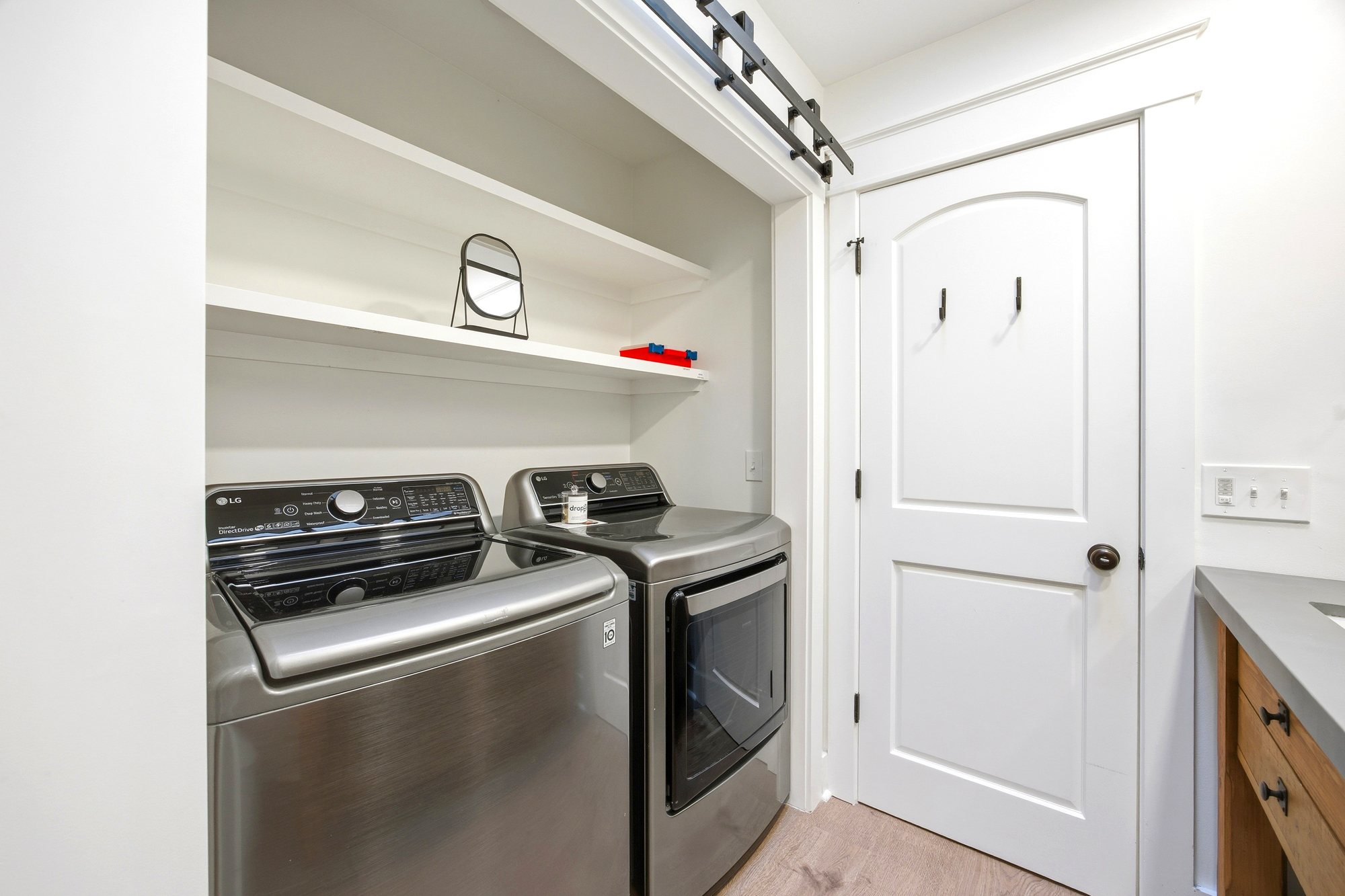Brushed steel appliances bring a modern, efficient pulse to this bright laundry nook. Tucked behind a sleek sliding barn door, the tidy shelving and airy atmosphere make everyday chores feel effortless and light.