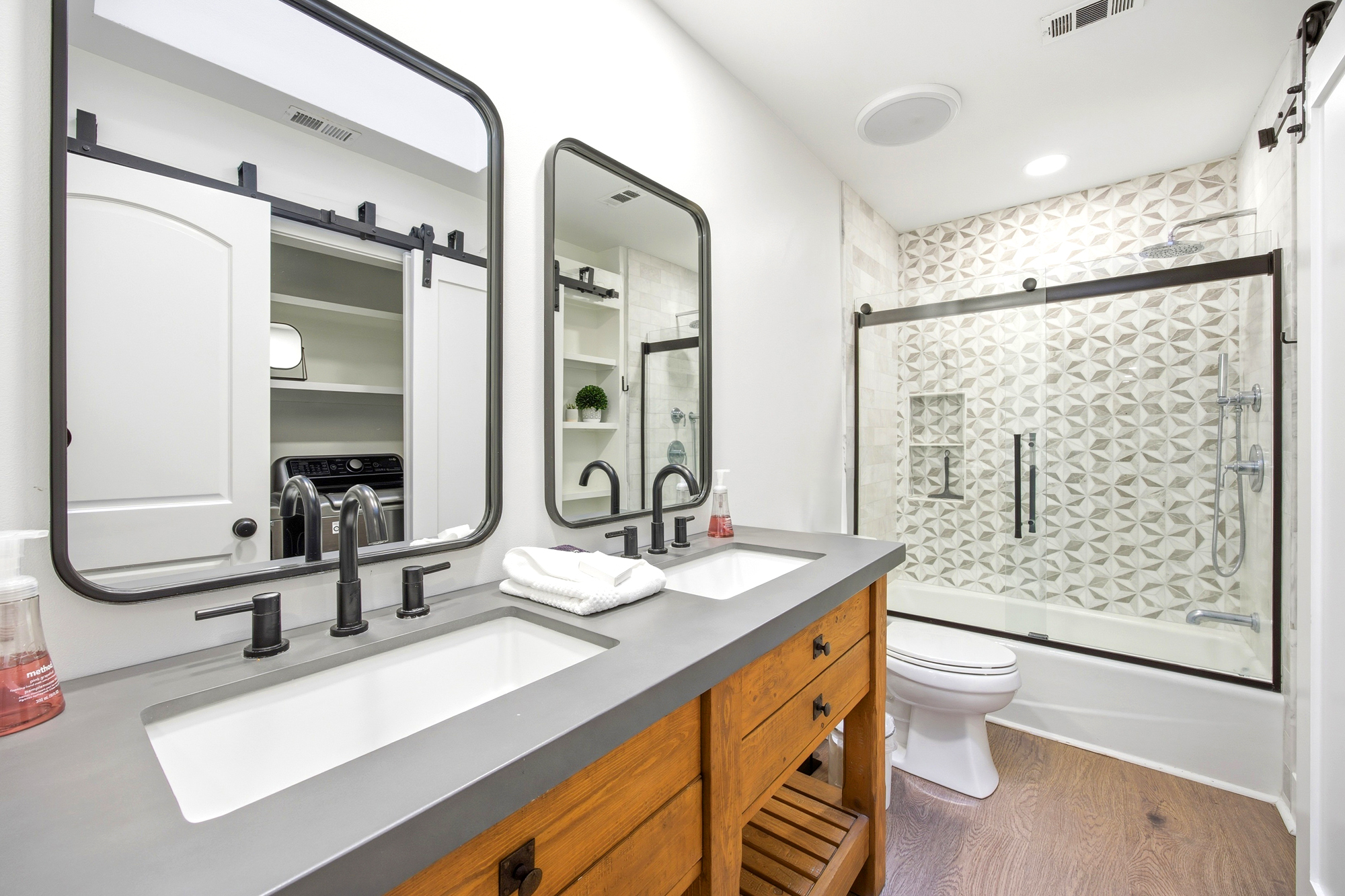 Geometric tiles and matte black accents create a sharp, modern contrast against the rustic wood vanity. This bright bathroom offers a spa-like atmosphere with its dual sinks and sleek glass shower enclosure.