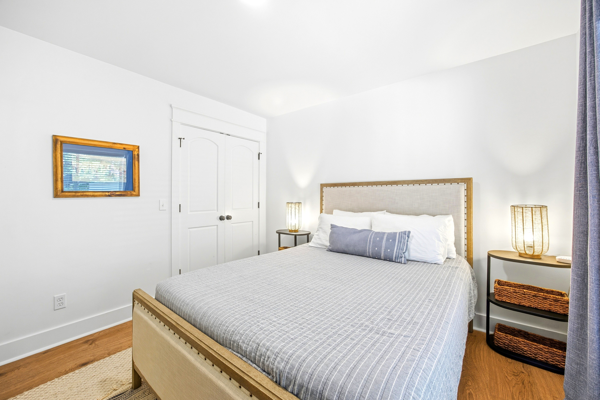 Woven textures and sea-inspired hues create a serene escape in this airy bedroom. Glowing lanterns flank the linen headboard, casting a gentle radiance across the crisp stripes and rich oak flooring.