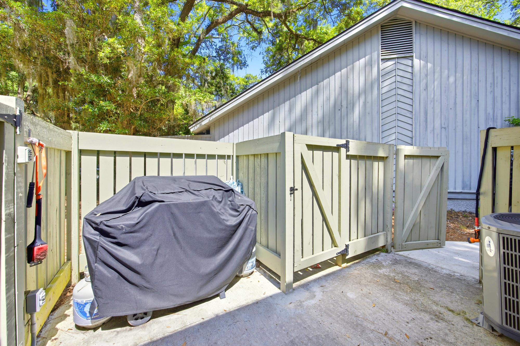 Sage-colored fencing encloses a private outdoor nook, where a pro-grade grill awaits your next barbecue. Towering oaks cast a dancing afternoon glow over the clean concrete patio, creating a quiet space for alfresco cooking in the fresh air.