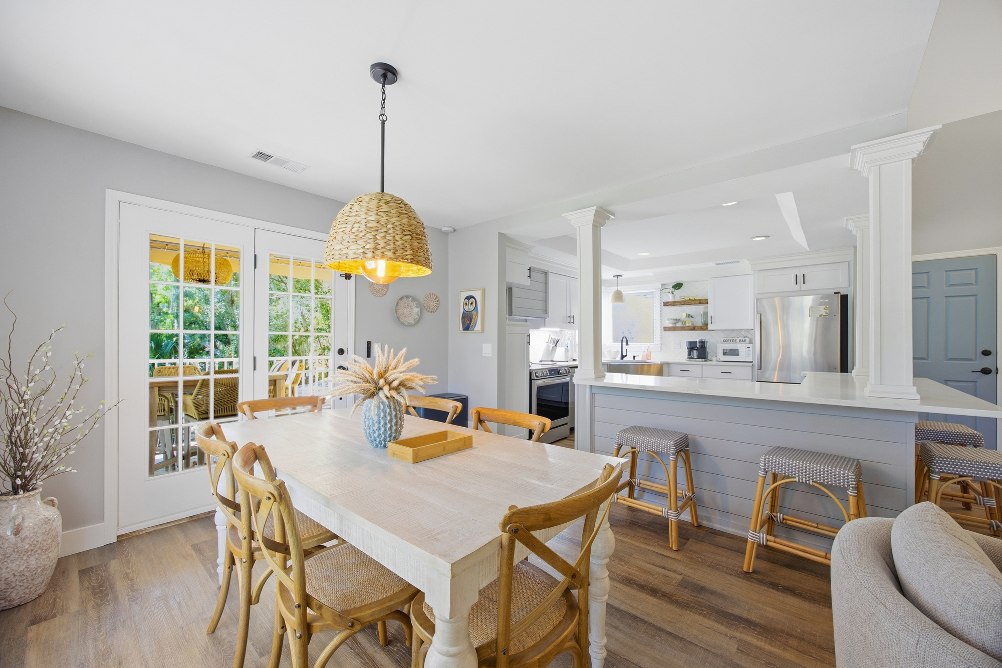 Natural wood tones and organic textures anchor this airy dining space, where a seagrass pendant casts a golden glow over morning coffee. French doors beckon you toward the leafy view, blending coastal charm with a seamless, open layout.