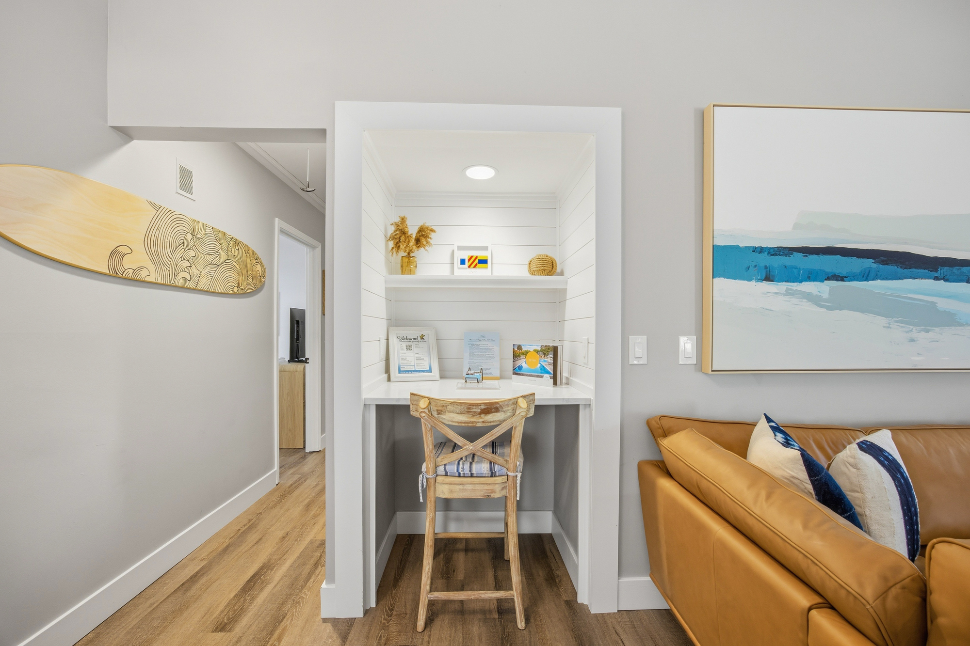 Coastal shiplap frames a quiet workspace, where a rustic wooden chair meets smooth surfaces. Surfboard art and leather textures create a calm, modern beach vibe that pairs perfectly with the steady glow of the recessed lighting.