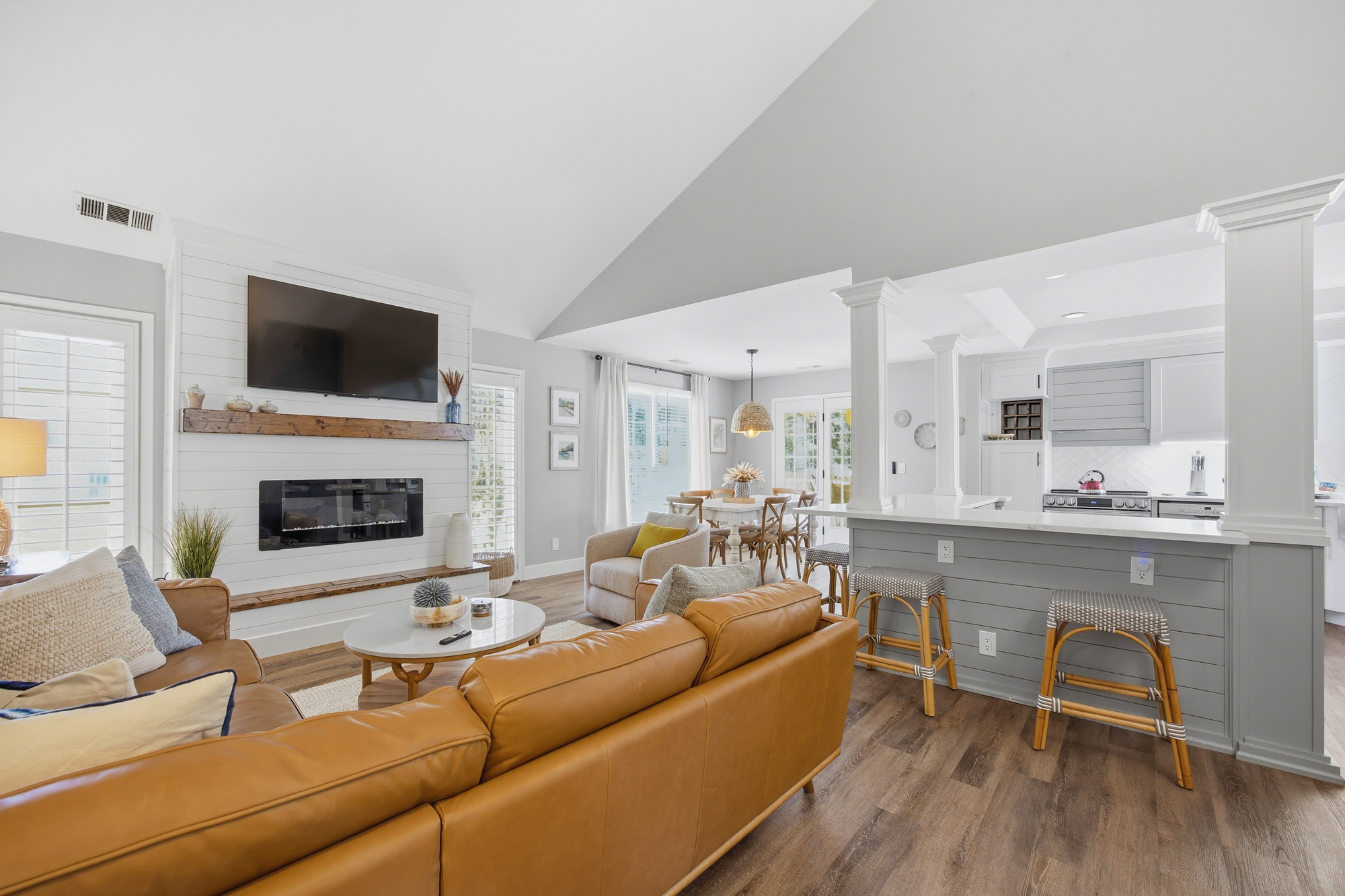 Amber leather seating anchors this airy open floor plan, where shiplap textures and dark wood mantels add rustic warmth. Soft daylight pours over the breakfast bar and hearth, creating a serene space for slow mornings and shared meals.