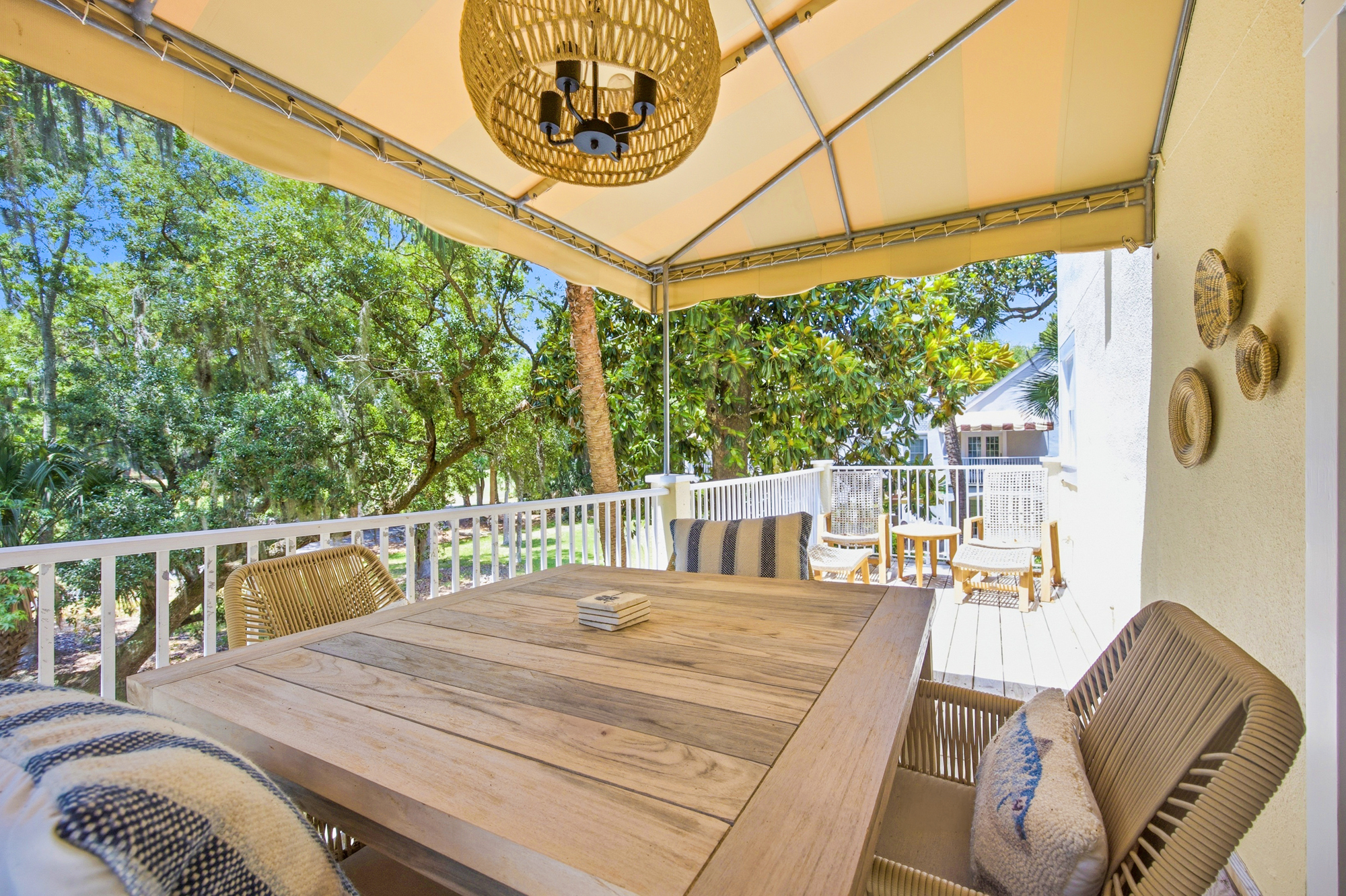 Striped awnings cast a warm glow over this elevated deck, where a raw wood table and wicker textures invite long alfresco lunches. Breezy views of the surrounding oak canopy create a quiet, shaded sanctuary for morning coffee or evening drinks.