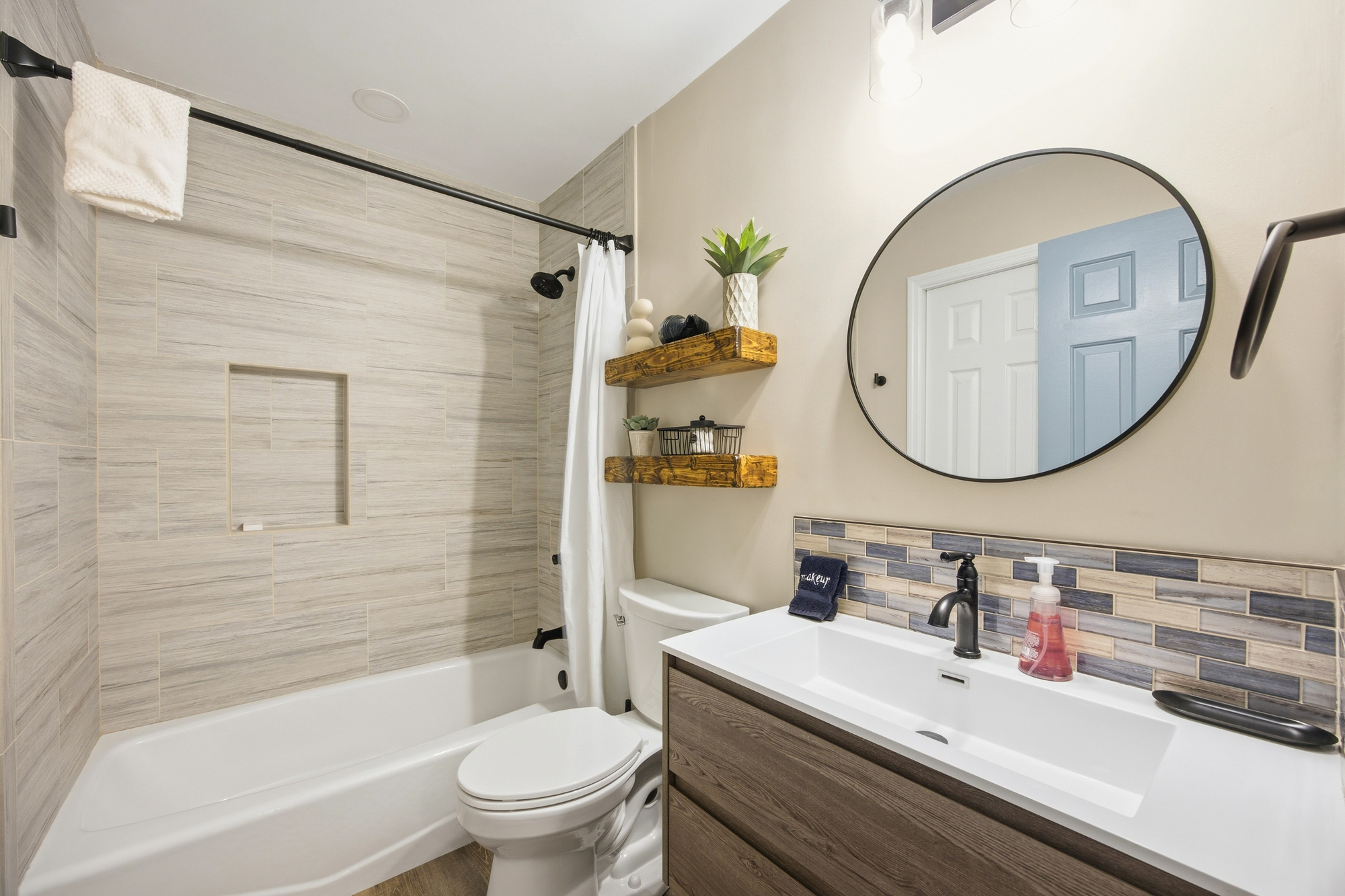 Textured tiling and floating wooden shelves bring an earthy, organic feel to this modern bathroom. A clean vanity with matte black accents creates a spa-like atmosphere for your morning routine.