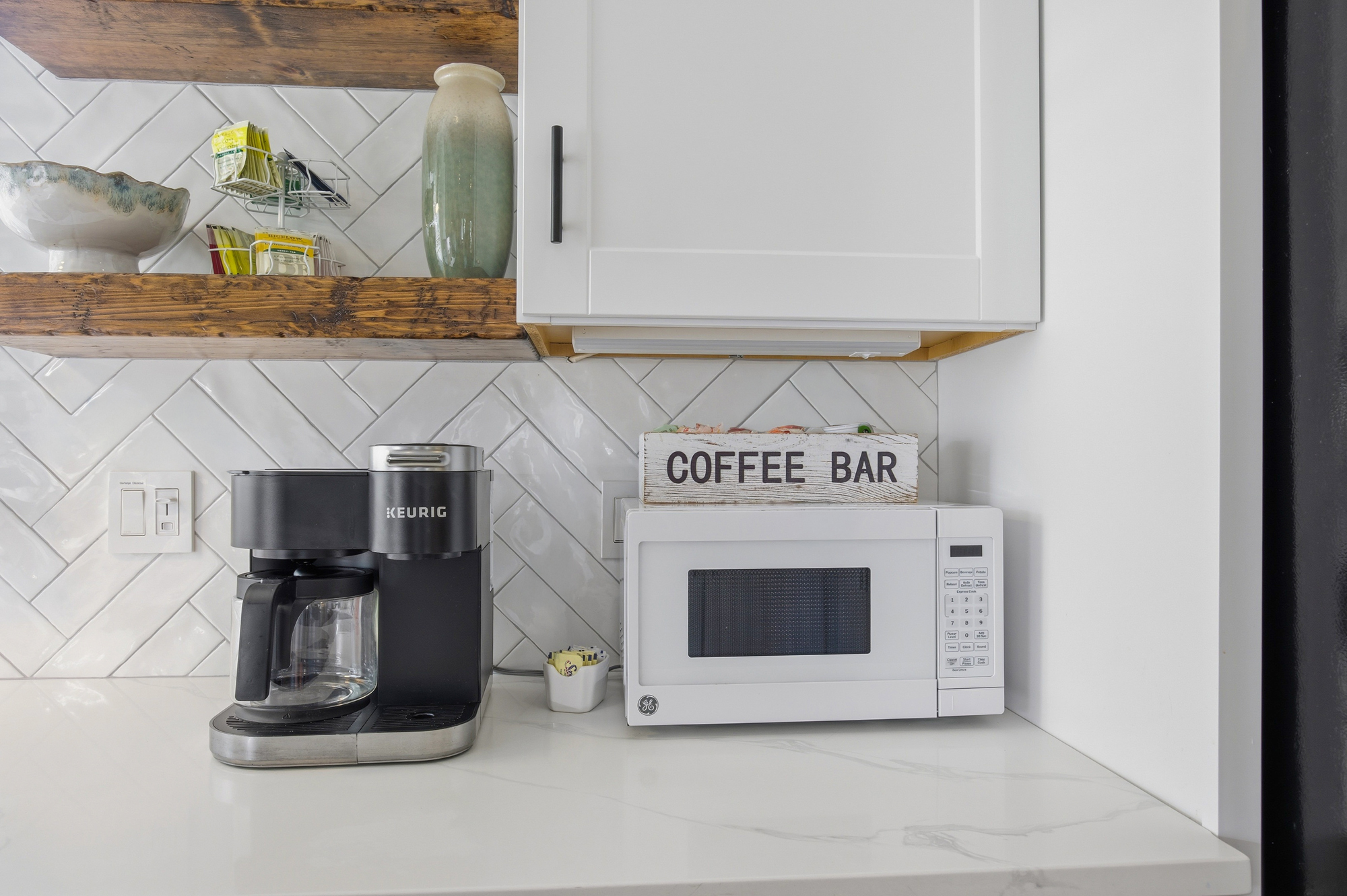 Reclaimed wood shelves and a classic herringbone backsplash create a textured backdrop for your morning routine. This charming coffee nook offers a dedicated space to brew a fresh cup and start your day in a bright, modern kitchen.