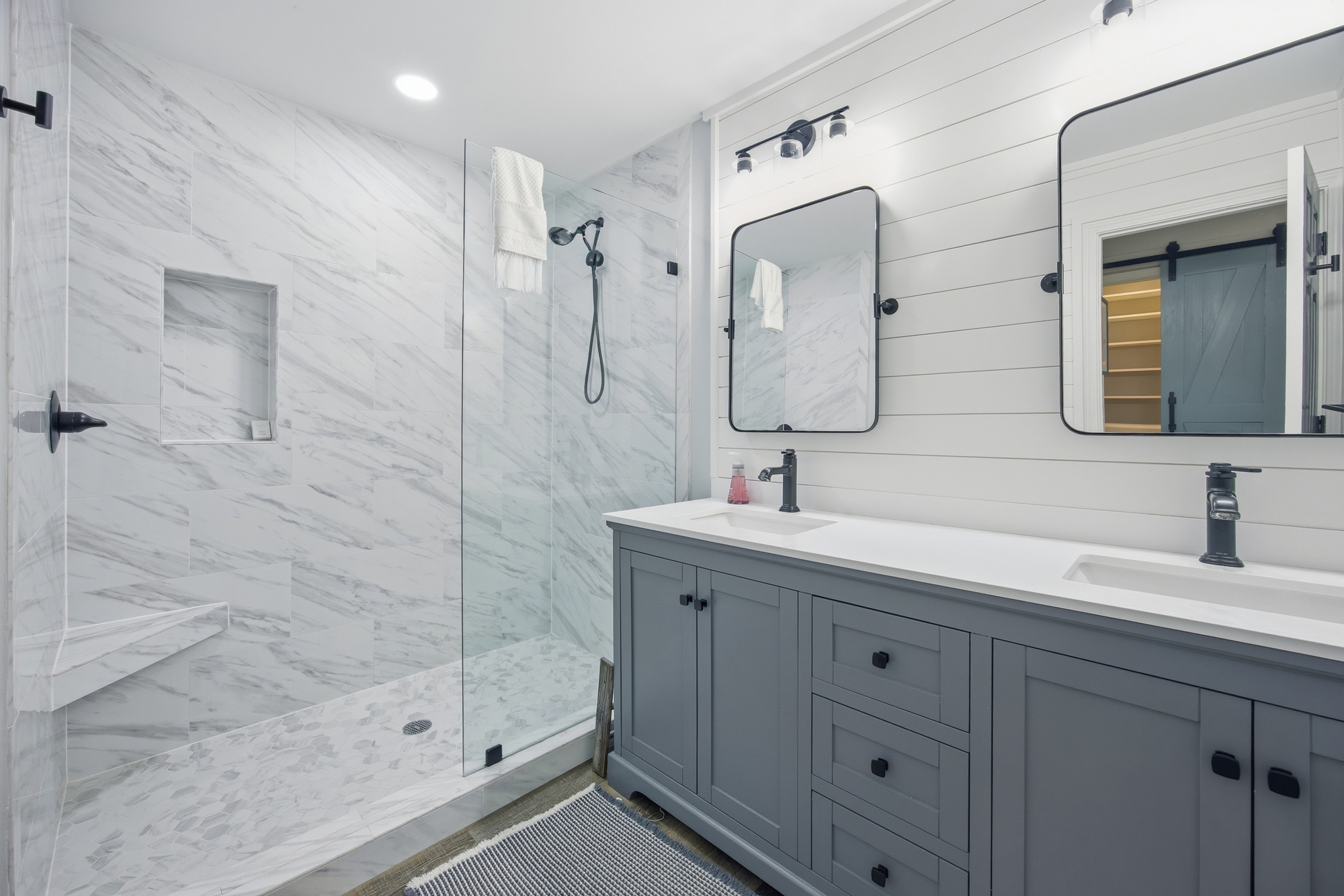 Cool marble tiles and sleek slate-gray cabinetry create a spa-like atmosphere for your morning routine. Bright, clean lines and matte black accents offer a modern, refreshing space to prepare for the day.