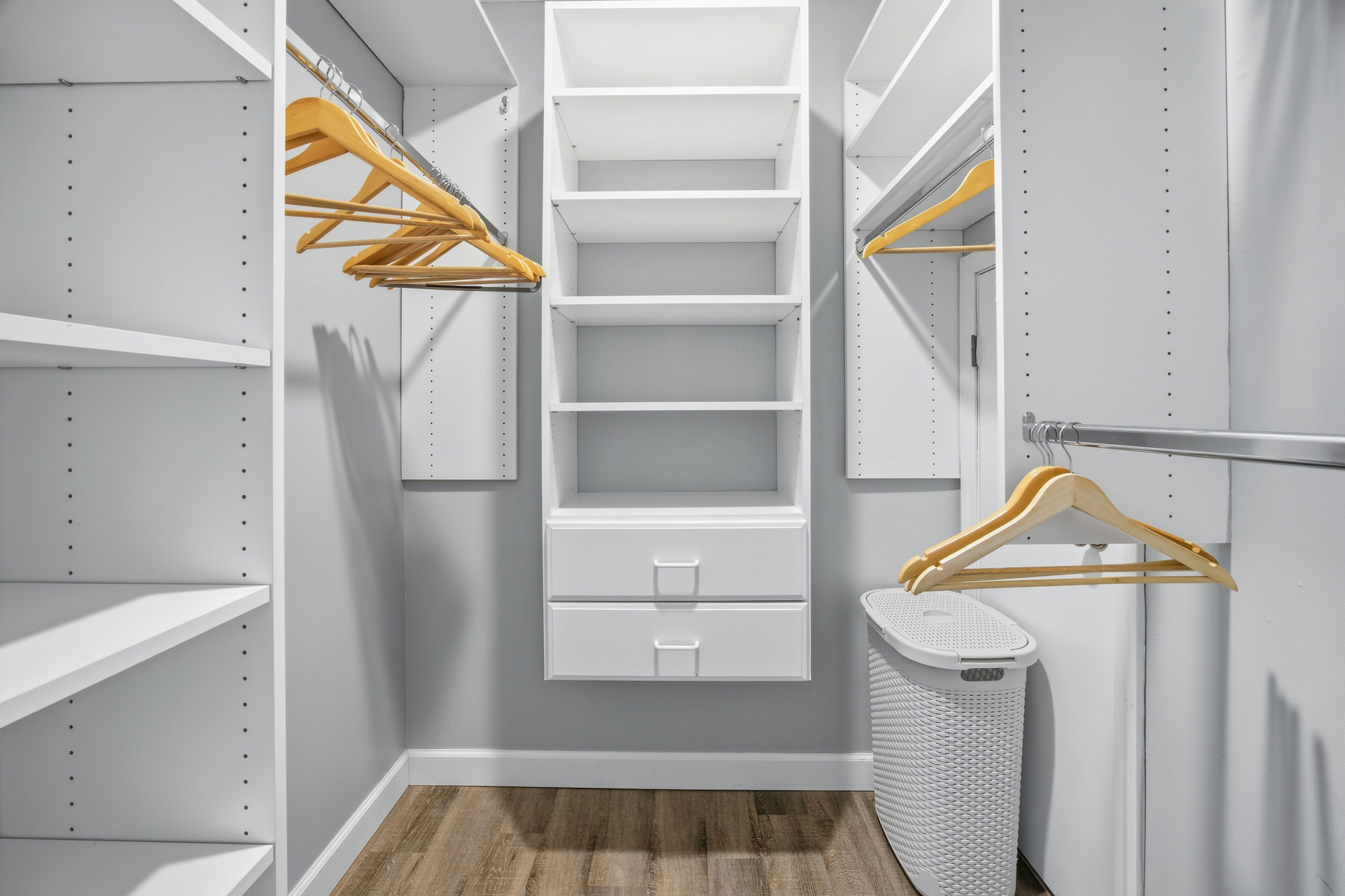 Polished wood hangers and crisp white shelving create a serene, organized space for your belongings. This expansive walk in closet features soft gray walls and warm flooring, providing a calm corner to prepare for your day.