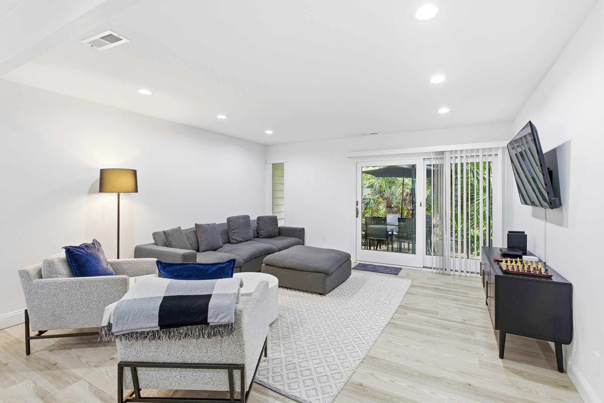 Plush charcoal seating and tactile fabrics create a cozy hub for movie nights or chess matches. Sliding glass doors draw in the lush green garden views, balancing the bright, minimalist interior with a breath of fresh air.