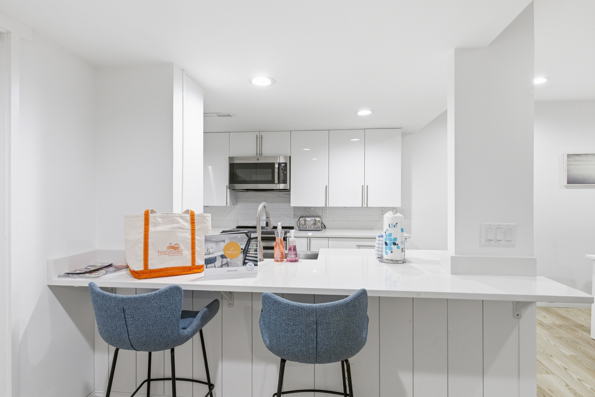 Crisp white cabinetry and quartz counters create a bright, airy culinary space perfect for slow mornings. Azure barstools add a pop of coastal color to this polished kitchen, where every detail feels fresh and impeccably clean.