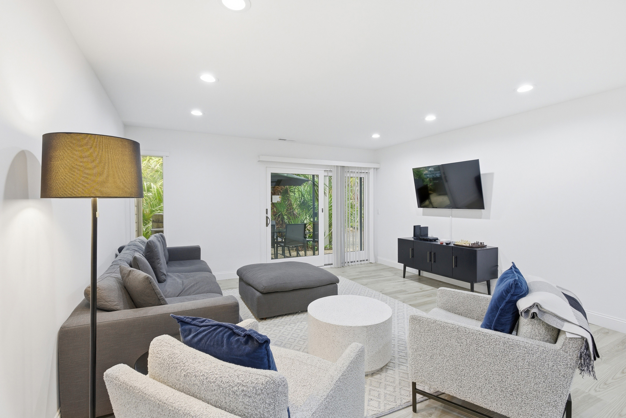 Textured armchairs and deep navy pillows anchor this bright, airy living room. Sliding glass doors pull the lush garden greenery inside, creating a peaceful backdrop for movie nights or quiet morning coffee in the soft glow of the recessed lights.