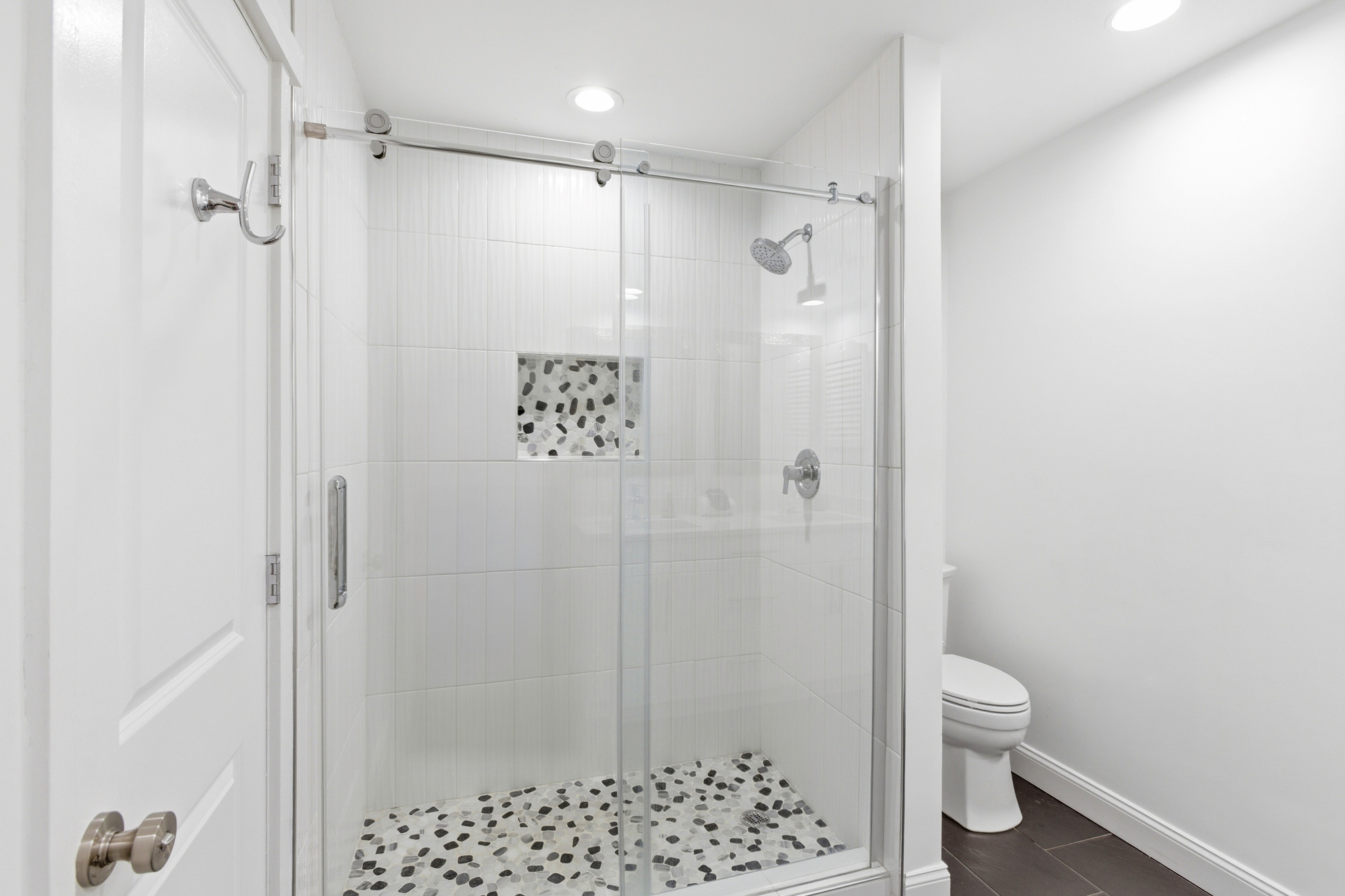 River stone floors and sleek glass doors create a serene, spa like atmosphere for your morning routine. Soft overhead glows highlight the clean vertical tiling and modern chrome finishes in this airy, minimalist bathroom.