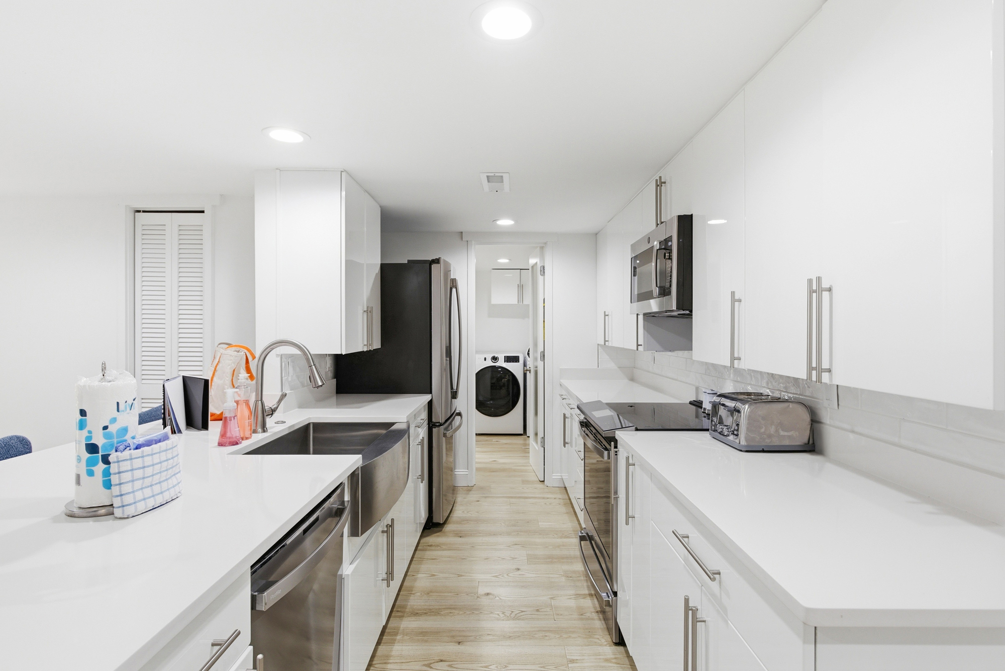 White quartz countertops and sleek minimalist cabinetry create a luminous, airy kitchen for shared meals. Stainless steel appliances and warm wood flooring ground the space, offering a clean and modern heart for your stay.