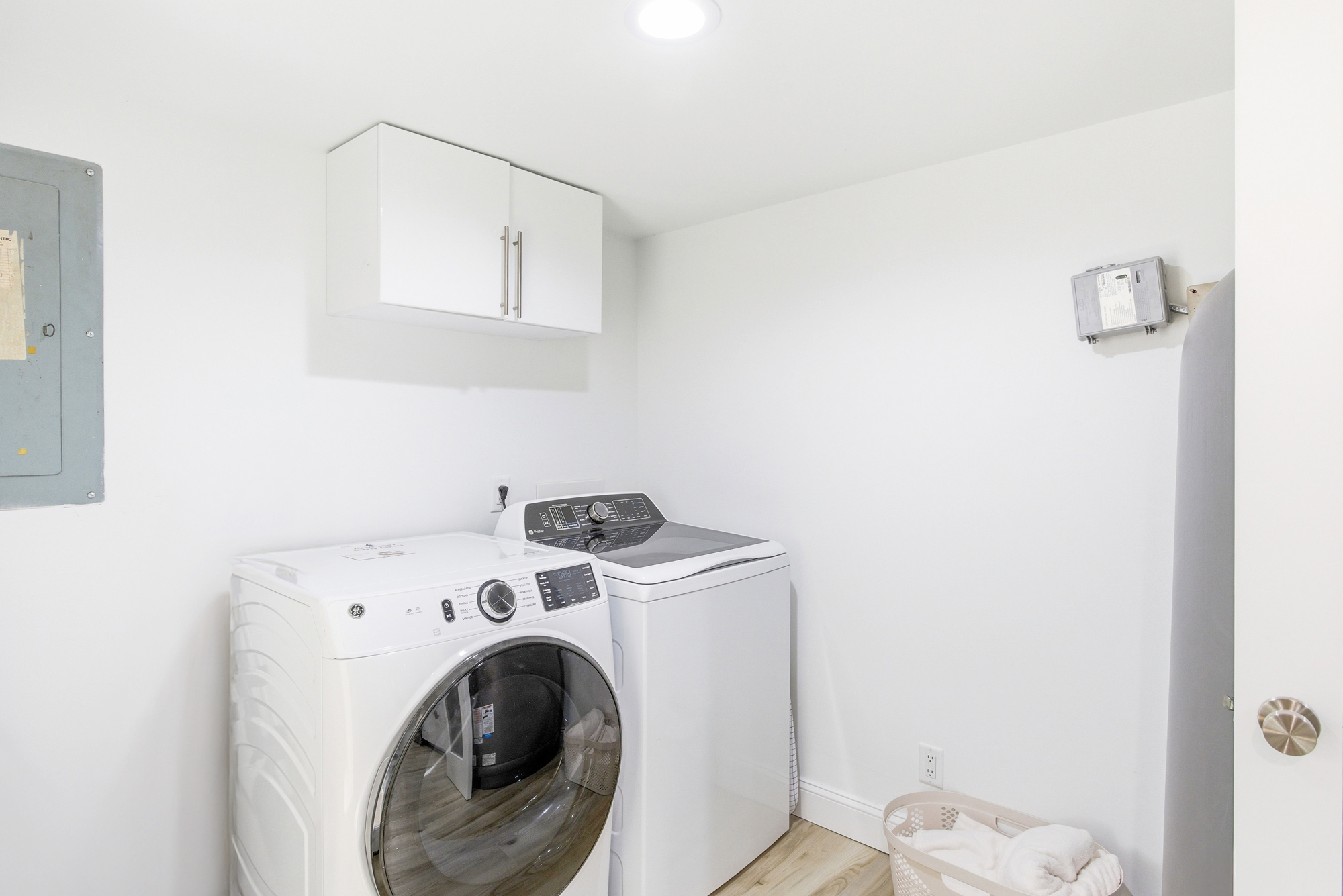 Fresh laundry awaits in this tidy utility nook, featuring modern machines and ample cabinetry. Warm wood-toned flooring and soft overhead glow make even the simplest chores feel effortless during your stay.