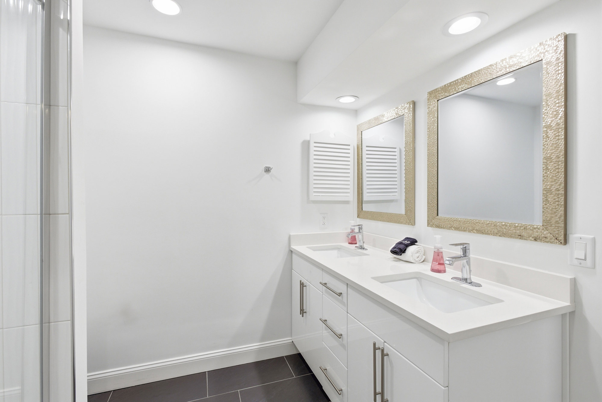 Gilded frames catch the soft overhead glow, adding a touch of glamour to this pristine double vanity. Deep charcoal floor tiles ground the airy space, creating a sleek and balanced environment for your morning routine.