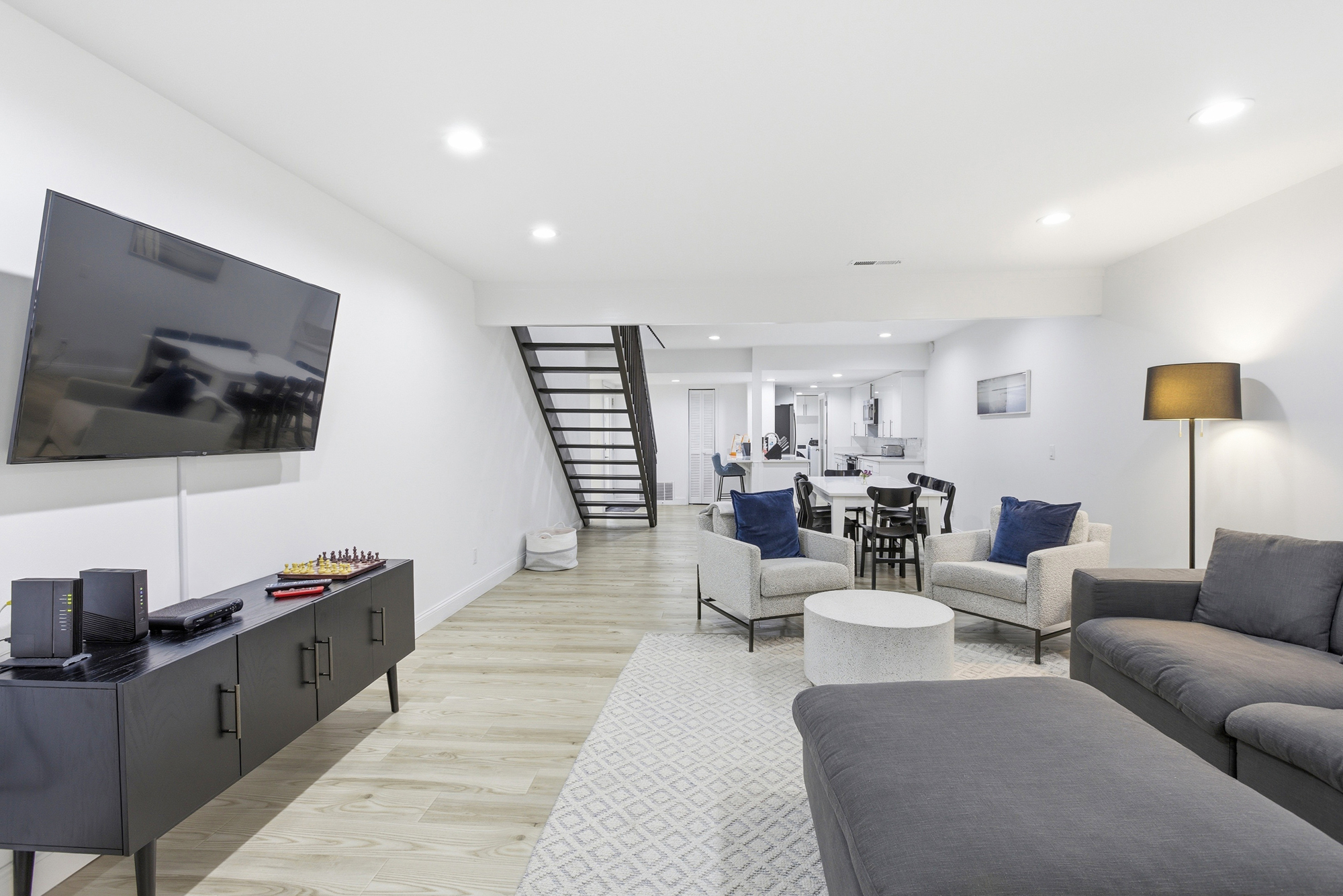 Deep navy accents and charcoal fabrics ground this airy, open living space. Clean architectural lines meet soft textures under a warm indoor glow, creating a sophisticated yet comfortable spot for movie nights or quiet morning coffee.