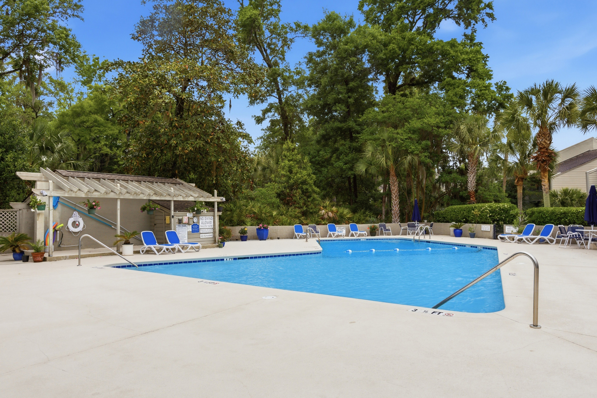 Turquoise waters shimmer under a vast blue sky, framed by the lush southern greenery and swaying palms of this peaceful poolside escape. Cool stone tiling and ample seating create an inviting spot for long, lazy afternoons in the midday glow.