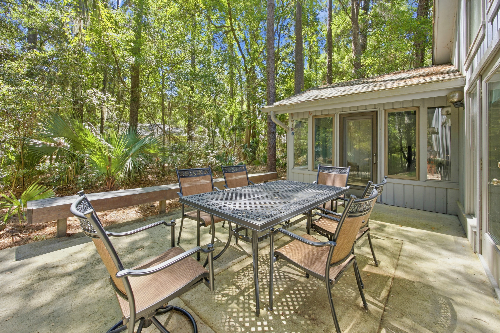 Dappled shadows dance across this stone patio, where a latticed iron table sits under a canopy of towering pines. It is a quiet spot for morning coffee or an alfresco dinner while surrounded by the lush, green textures of the forest.