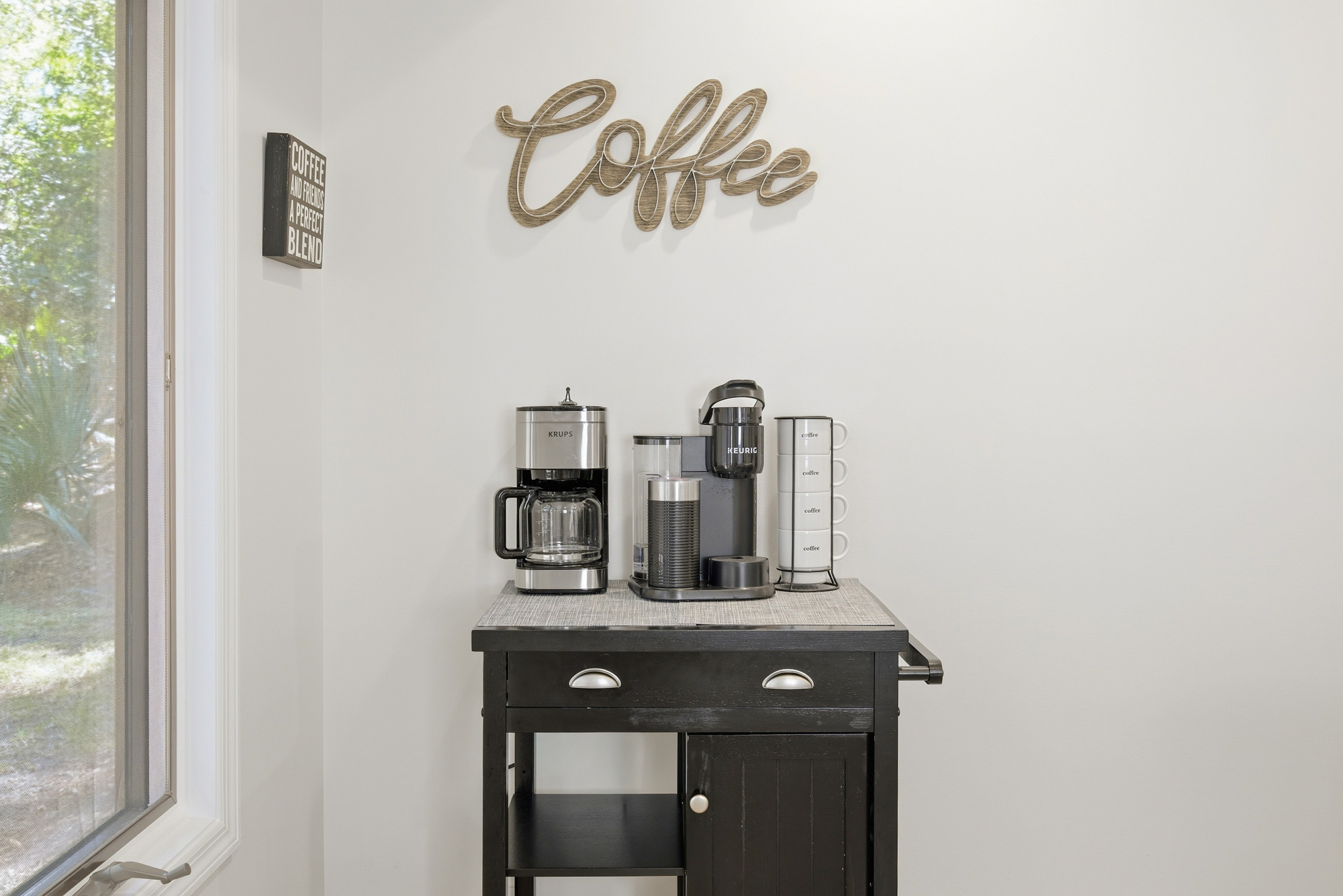Steel and wood accents define this cozy beverage station, where the morning glow pours through the window to meet your caffeine ritual. White mugs stand ready for a fresh brew atop a dark, elegant cart for a perfect start to your day.