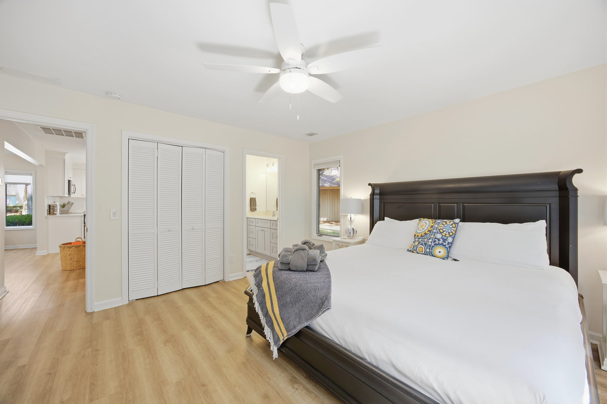 Soft white linens and a stately dark wood frame anchor this airy bedroom, where morning rays catch the smooth grain of the oak floors. A patterned pillow adds a playful pop of color to the serene, open space.