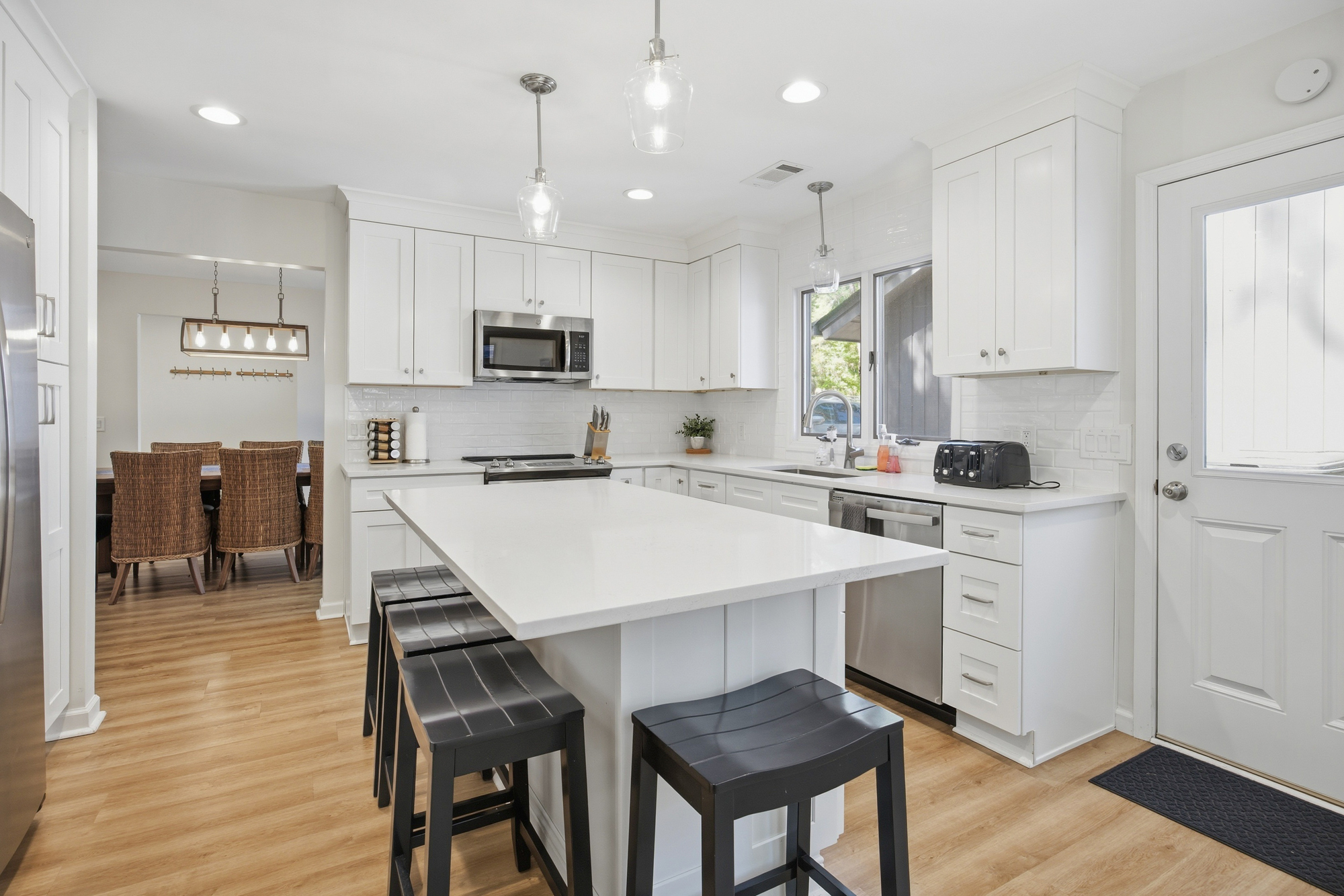Alabaster countertops and sleek cabinetry create a luminous culinary space, perfect for slow mornings. Glass pendants glow above the island, while the open layout invites easy conversation between the kitchen and the textured dining area beyond.