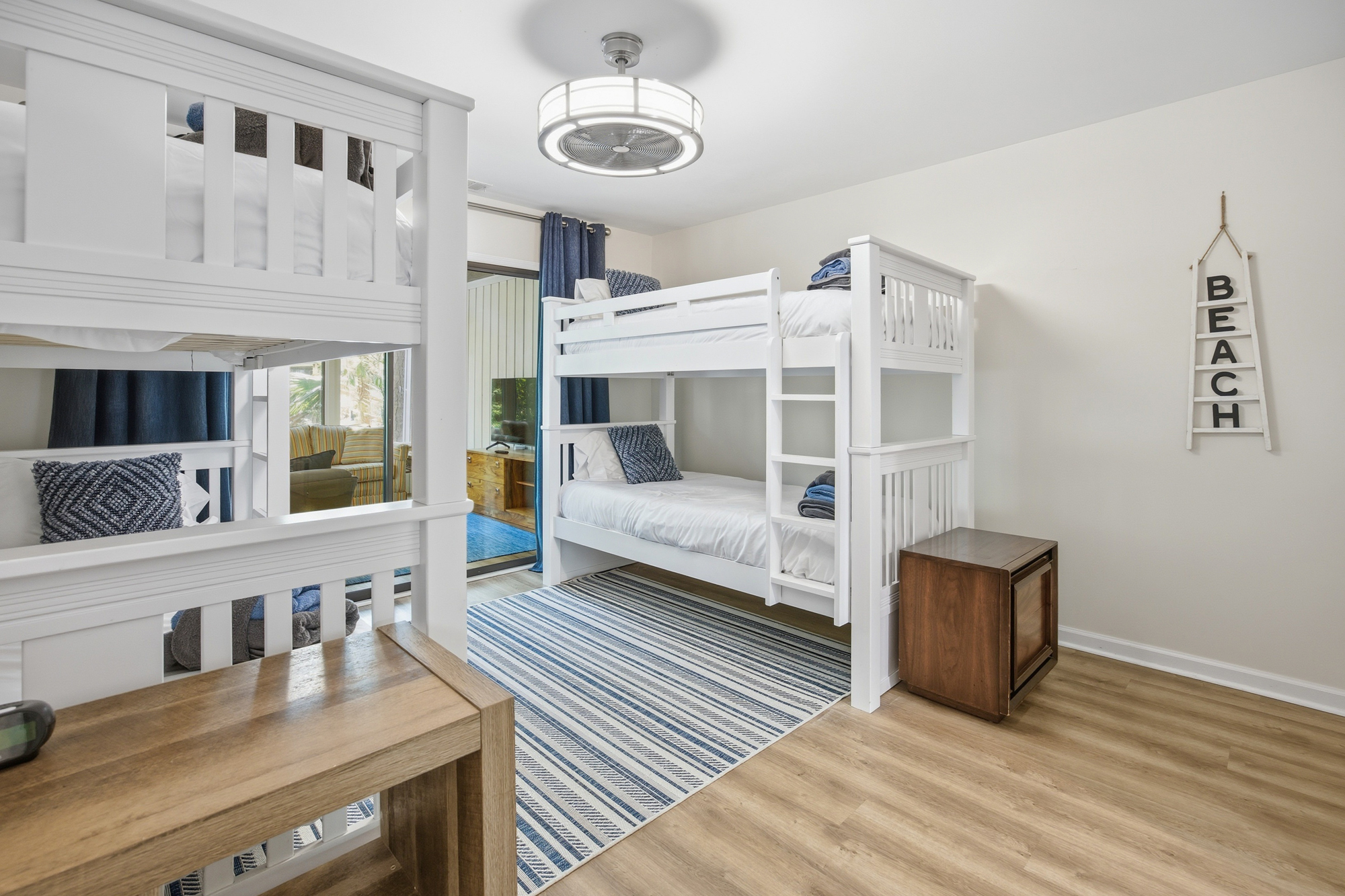 Nautical stripes and bright white bunk beds create a cheerful, airy space for the whole family. Soft daytime light catches the warm wood flooring and coastal decor, making this a cozy spot for children to dream after a day in the sand.