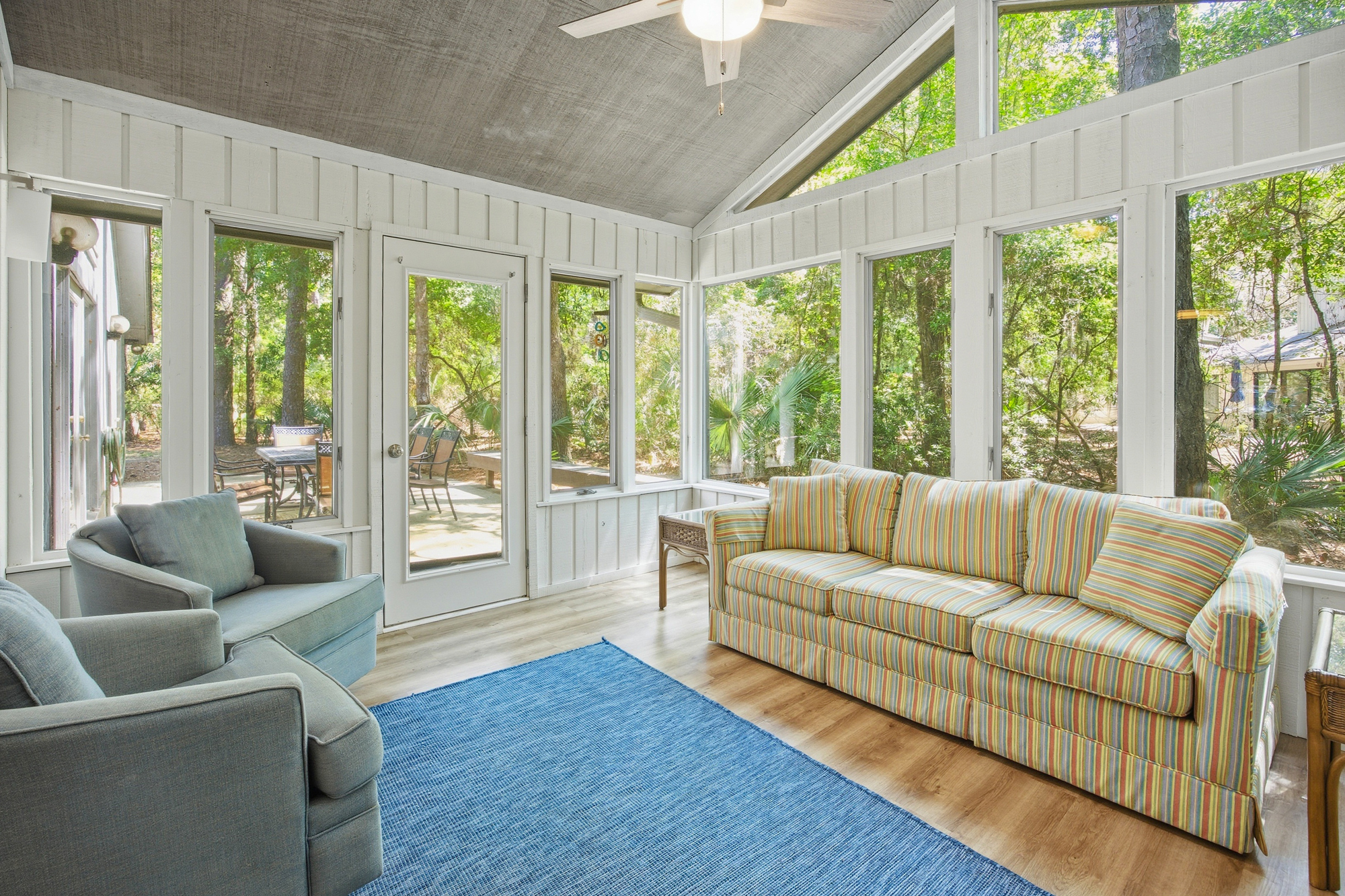 Floor to ceiling windows pull the lush forest greenery right into this airy sunroom. Light wood floors and soft, striped seating create a breezy spot to watch the shadows dance across the trees.