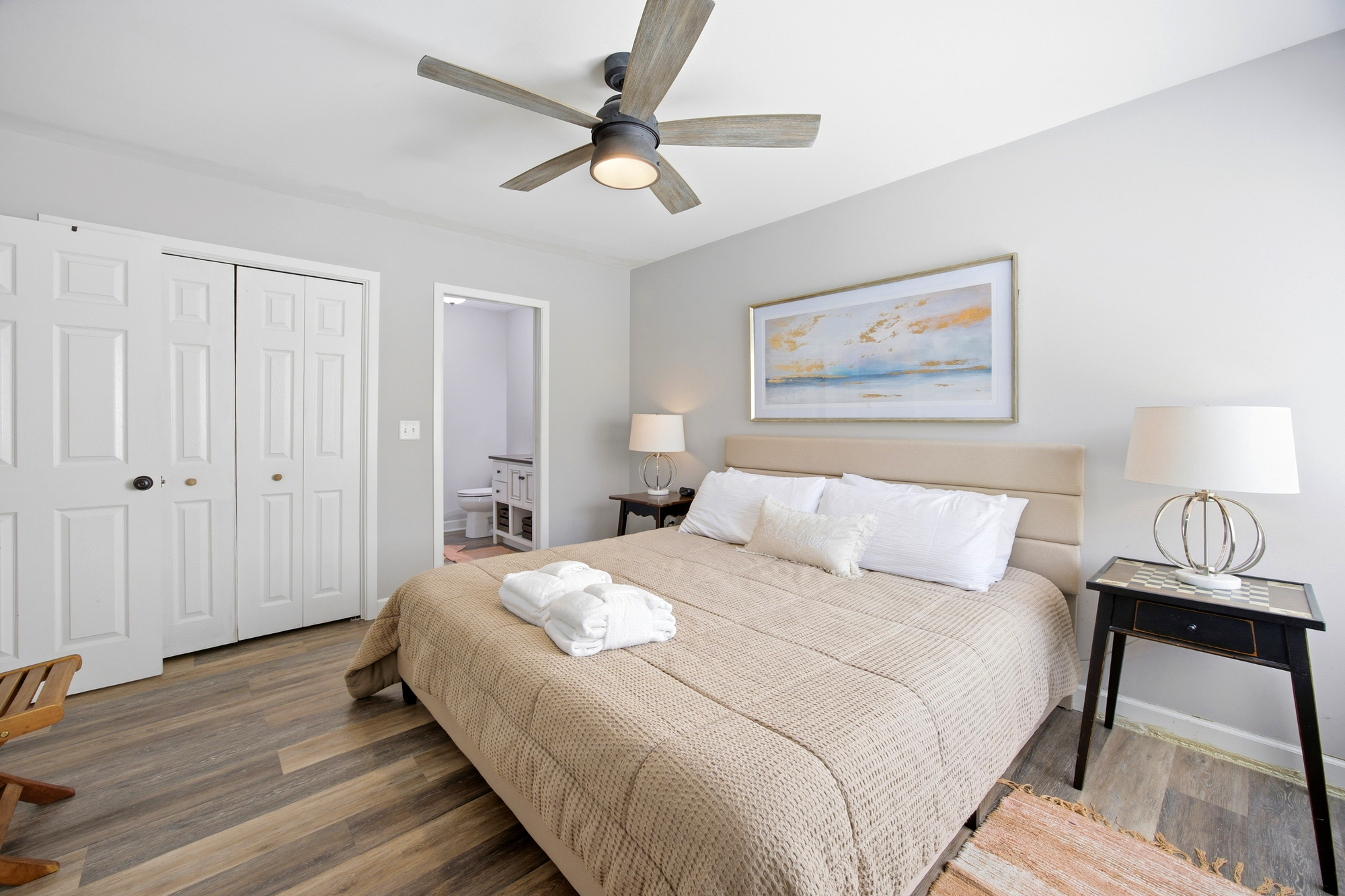 Honey-toned linens and plush robes wait atop the bed, creating a cozy sanctuary for a restful night. A gentle breeze from the timber-bladed fan cools the airy suite, while golden accents on the walls catch the midday glow.