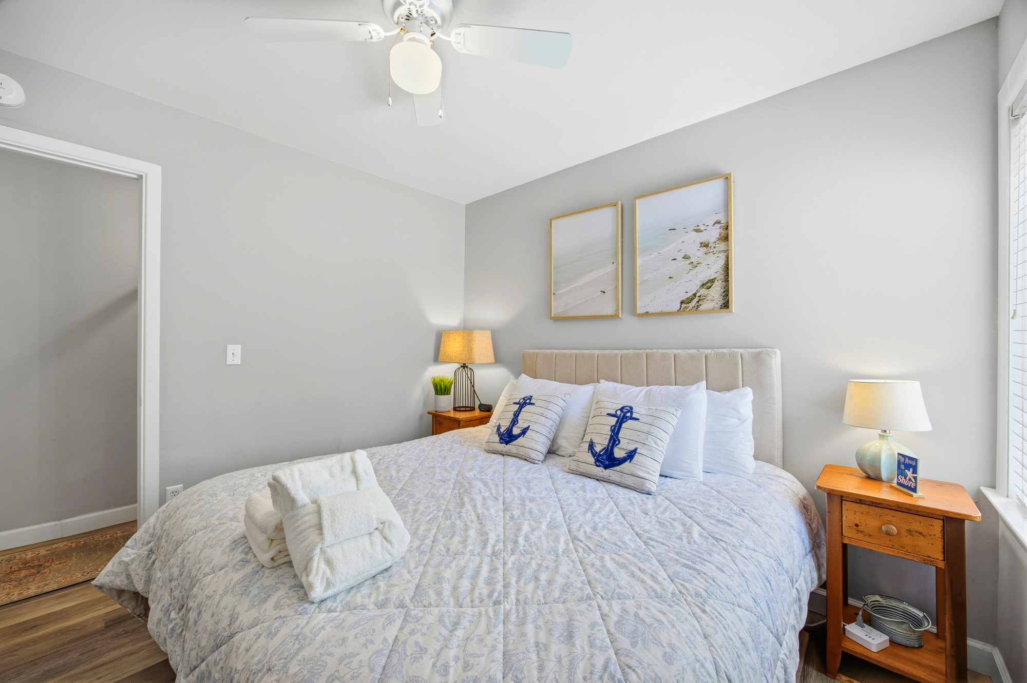Nautical accents and quilted linens create a serene coastal sanctuary. Warm bedside lamps cast a golden radiance across the plush pillows and wooden textures, offering a peaceful space to rest after a day by the sea.