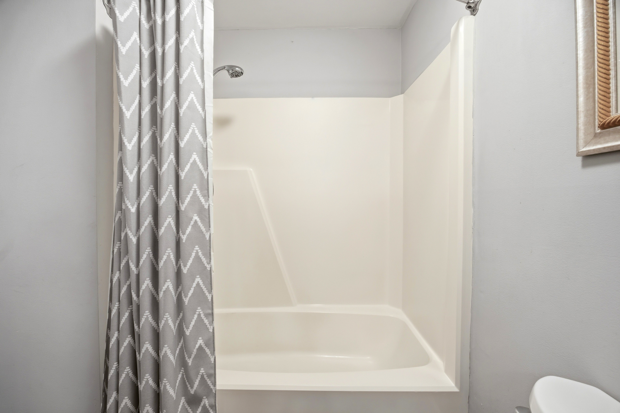 Geometric patterns on a slate gray curtain bring a modern touch to this bright bathroom. A deep tub and sparkling chrome fixtures create a clean, refreshing space to prepare for your day.
